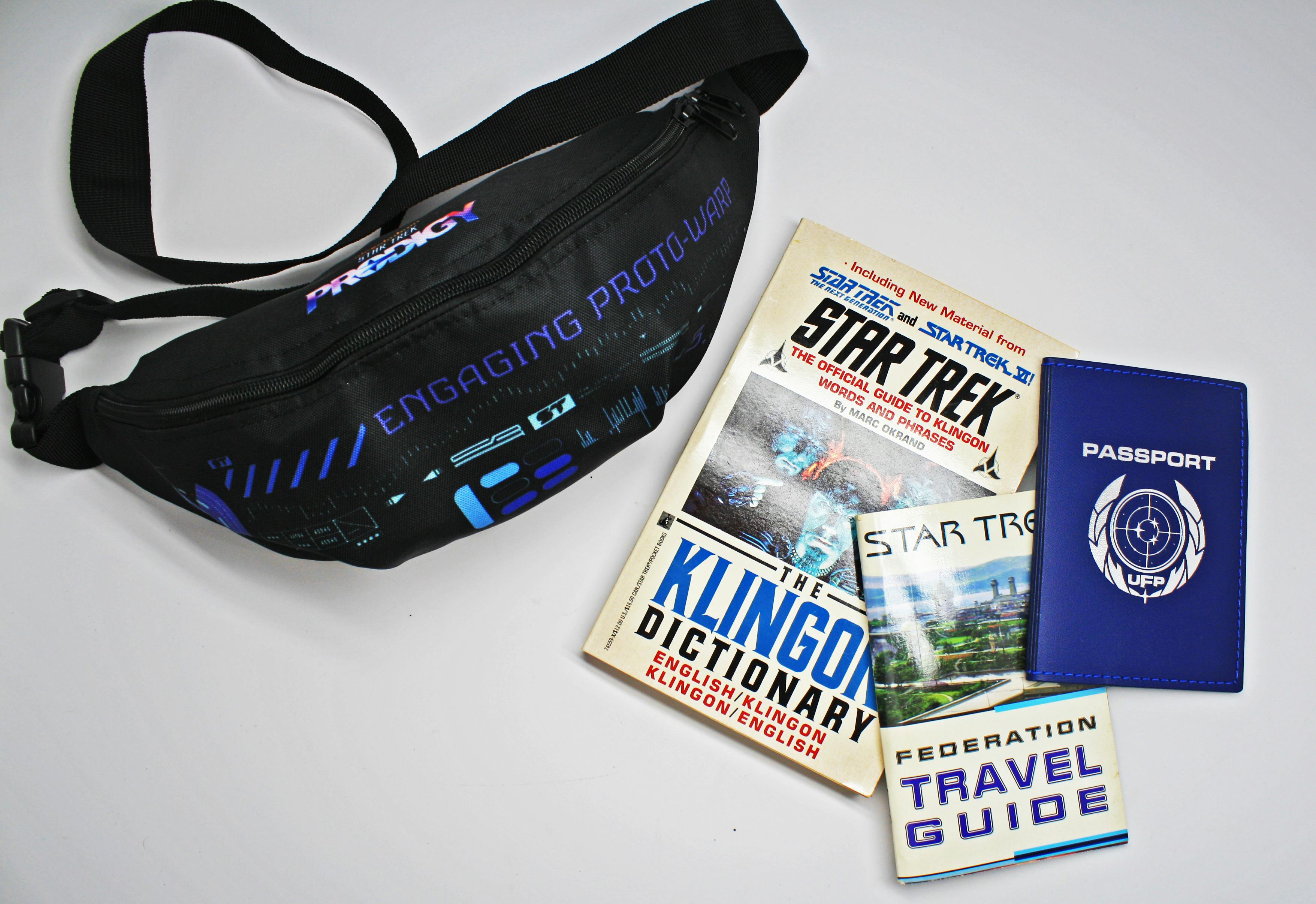 Flat lay of a Star Trek: Prodigy fanny pack, Klingon dictionary, Federation travel guide, and UFP passport