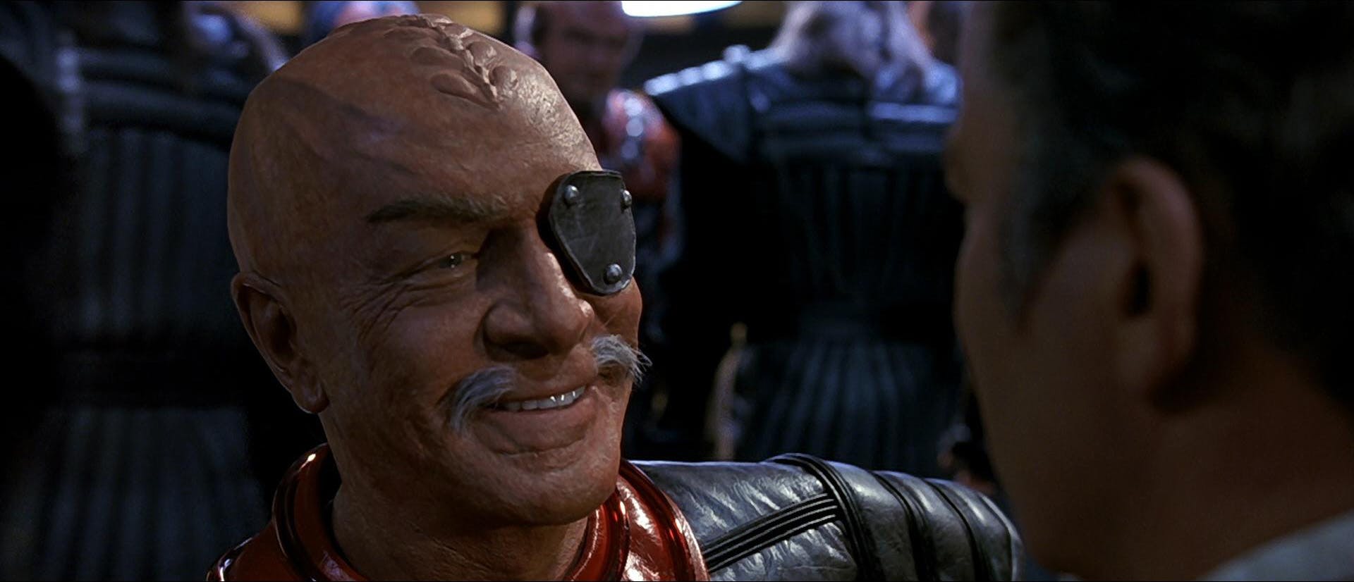 General Chang, standing in front of James Kirk, smiles a dastardly smile, before beaming off the Enterprise with their Klingon crew in Star Trek: The Undiscovered Country