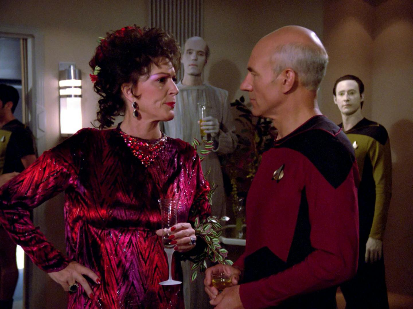 At a gathering, Lwaxana Troi speaks privately with Captain Picard with her hand on her hip as Data observes in 'Haven'