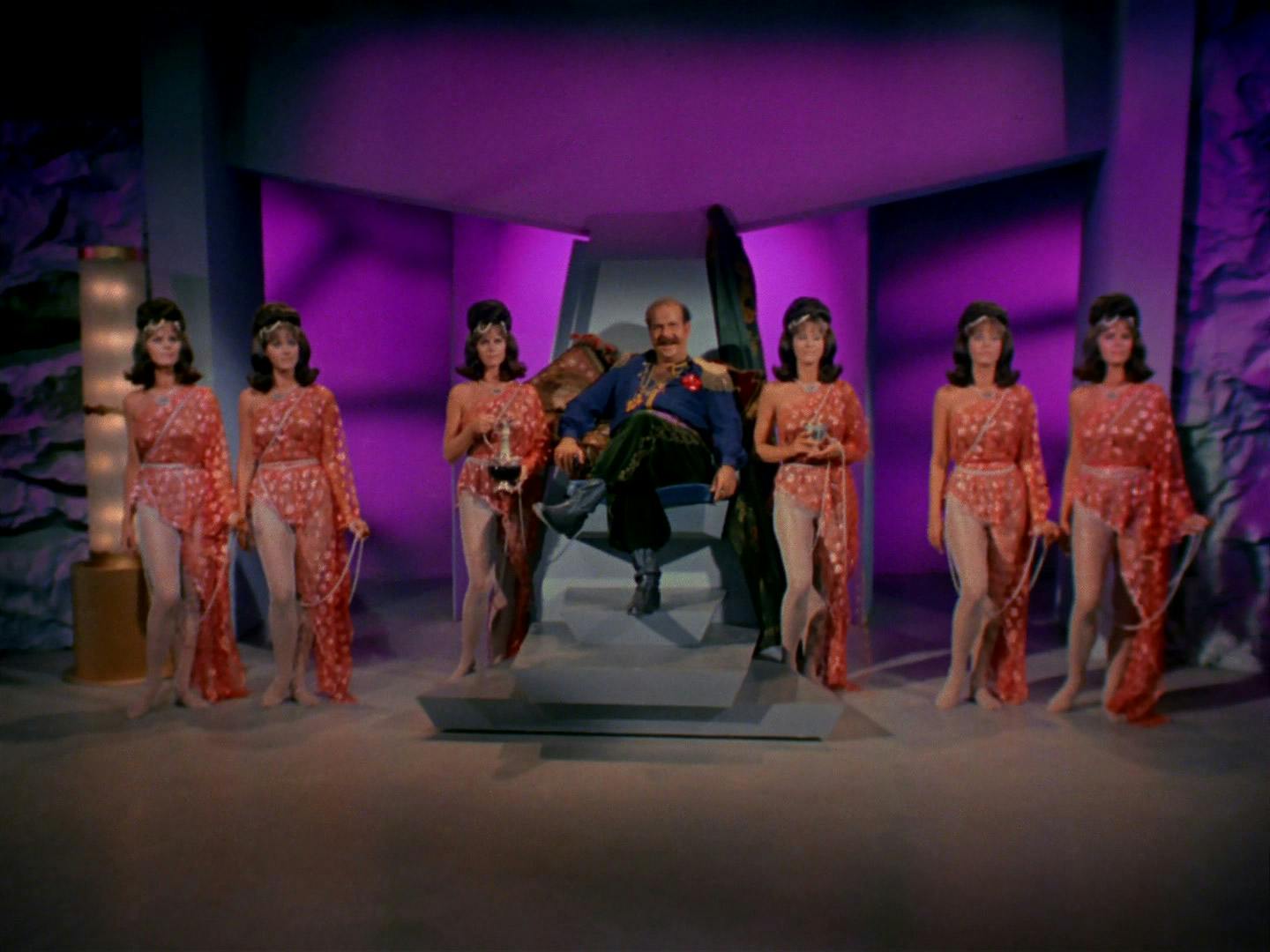 Harry Mudd sits on his throne with his legs crossed, flanked by his six identical androids in 'I, Mudd'