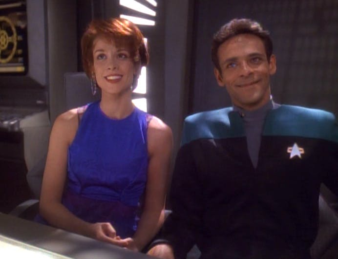 Sitting side-by-side at a conference room table, Leeta and Bashir look up towards Jadzia Dax with wide grins in 'Facets'