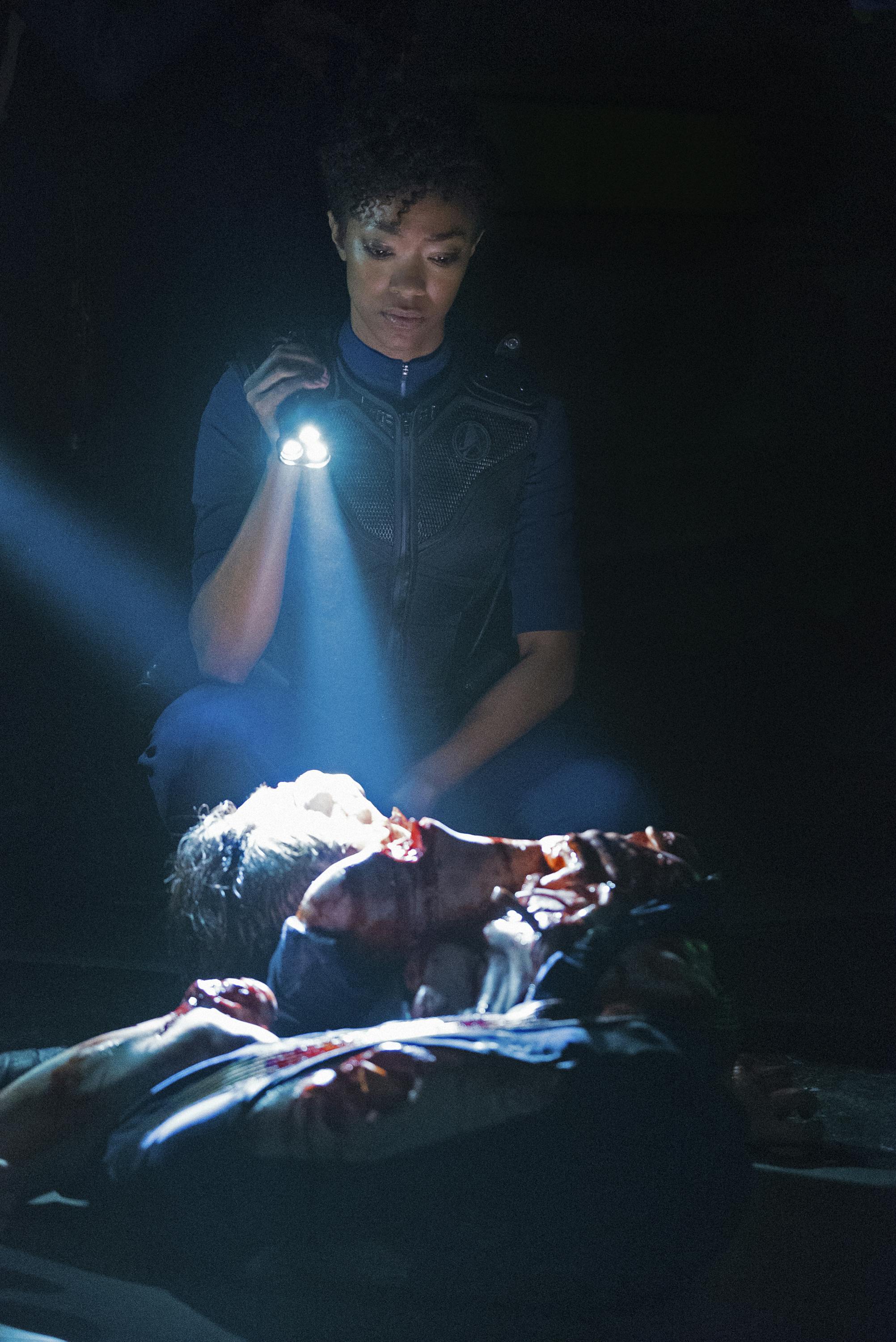 Aboard the Glenn, Michael Burnham shines a flashlight and kneels beside the mauled bodies of the crew in 'Context is for Kings'