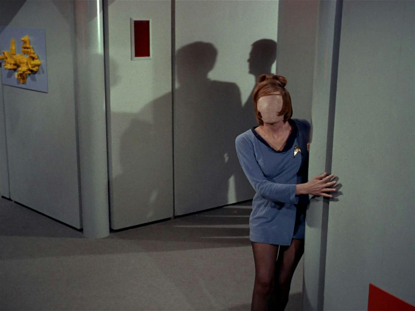 A Starfleet officer rounds the corner of an Enterprise corridor clinging to the wall as she no longer has a face in 'Charlie X'