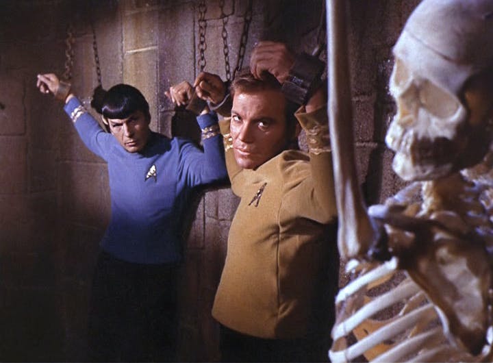 Spock and Kirk chained to the wall look over to their cellmate, a skeleton, in 'Catspaw'