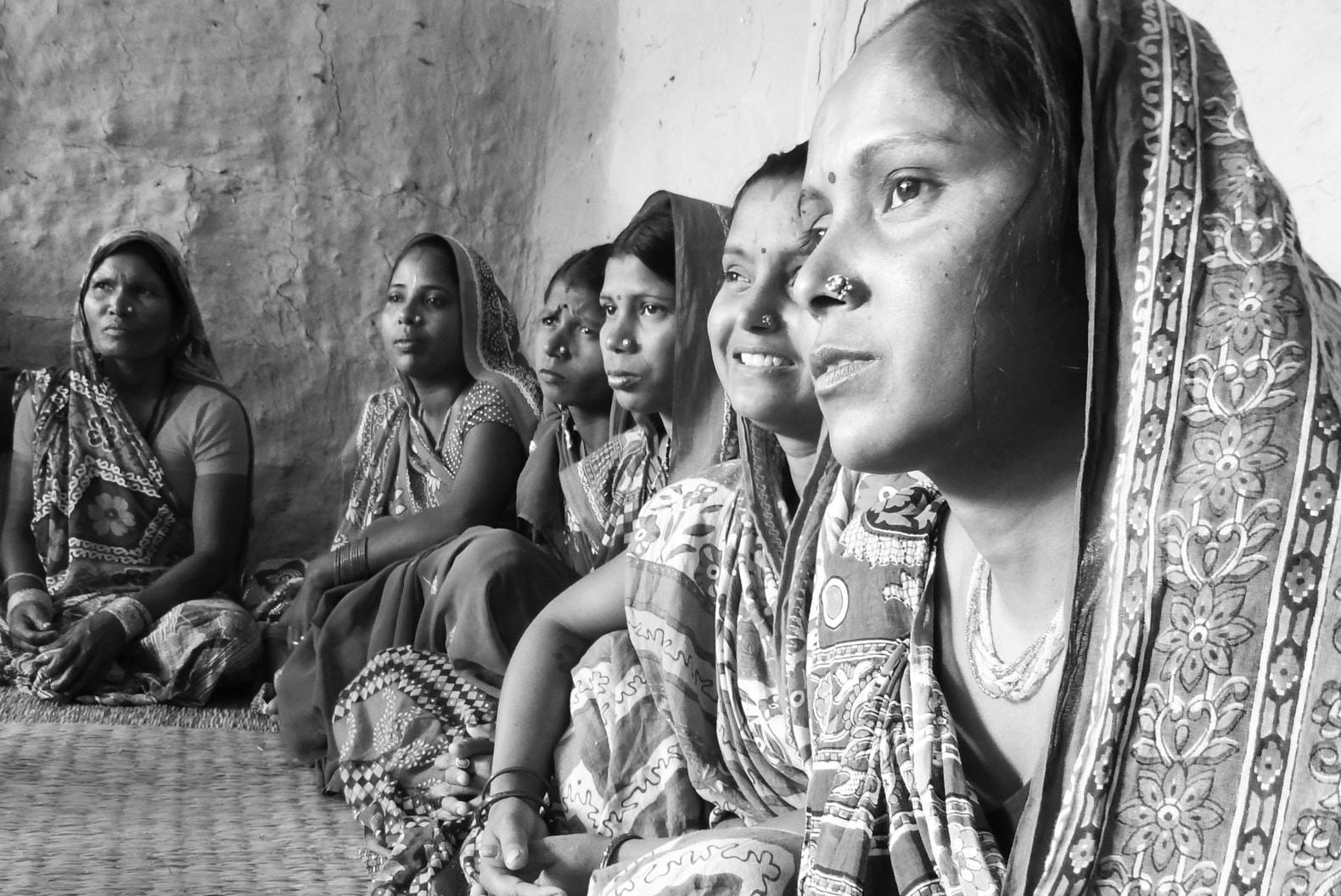 A group of women with scarves sit around a floor.