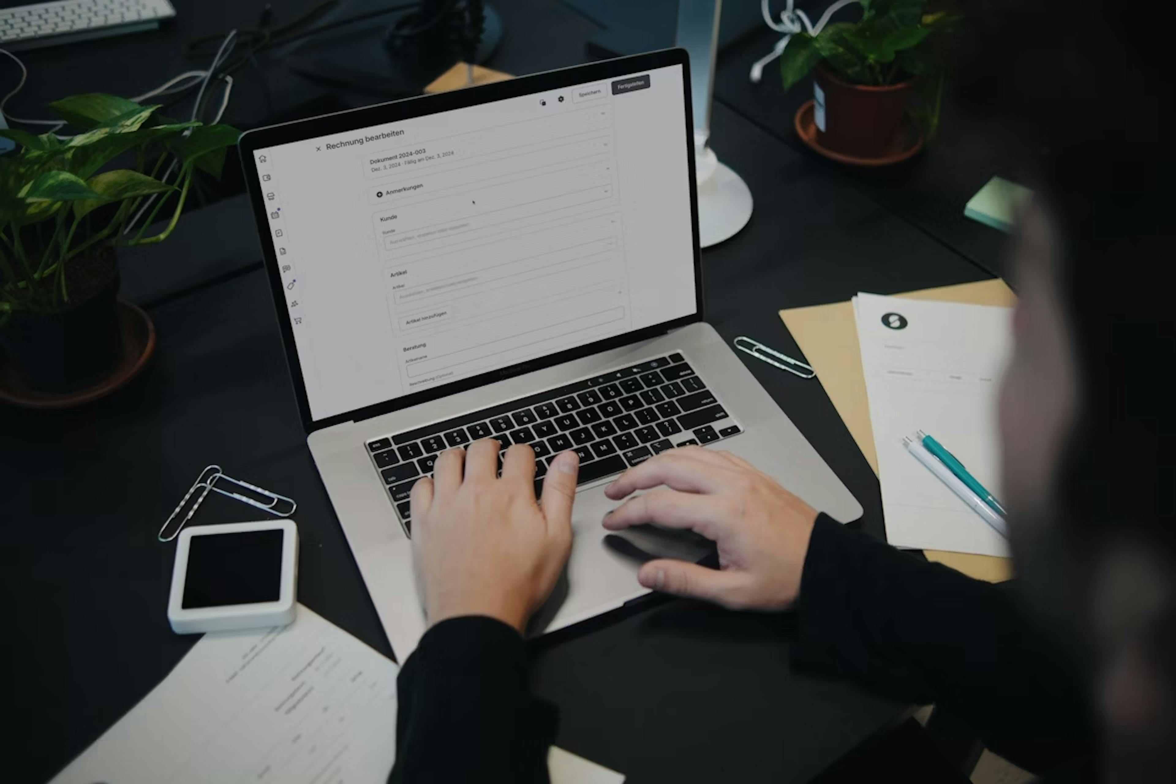 Photo of a person using a laptop with invoices and POS