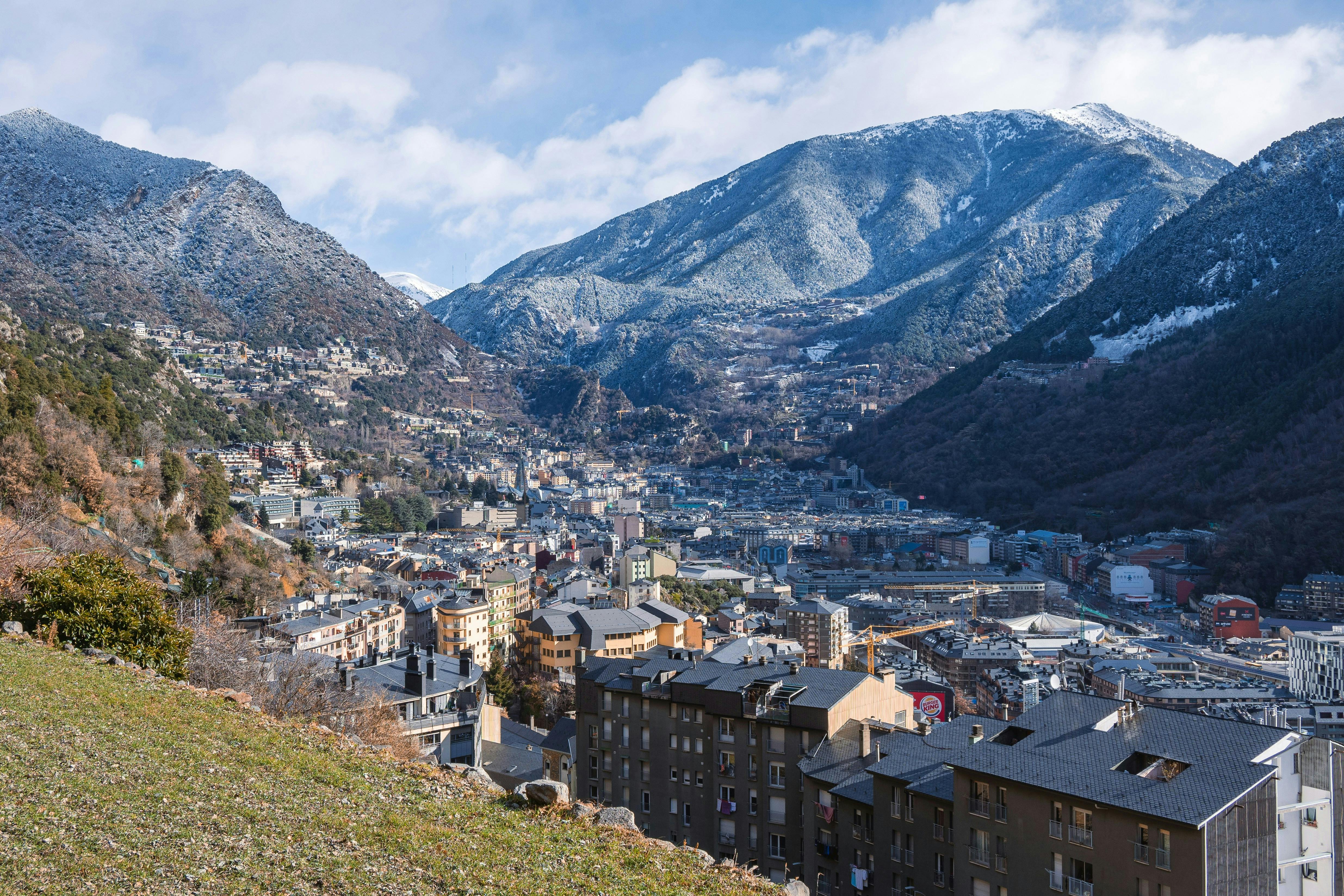 An aerial view of andorre-la-vieille in Andorra. The image shows a cluster of buildings spread across the valley, surrounded by mountains. The mix of natural beauty and urban structures.