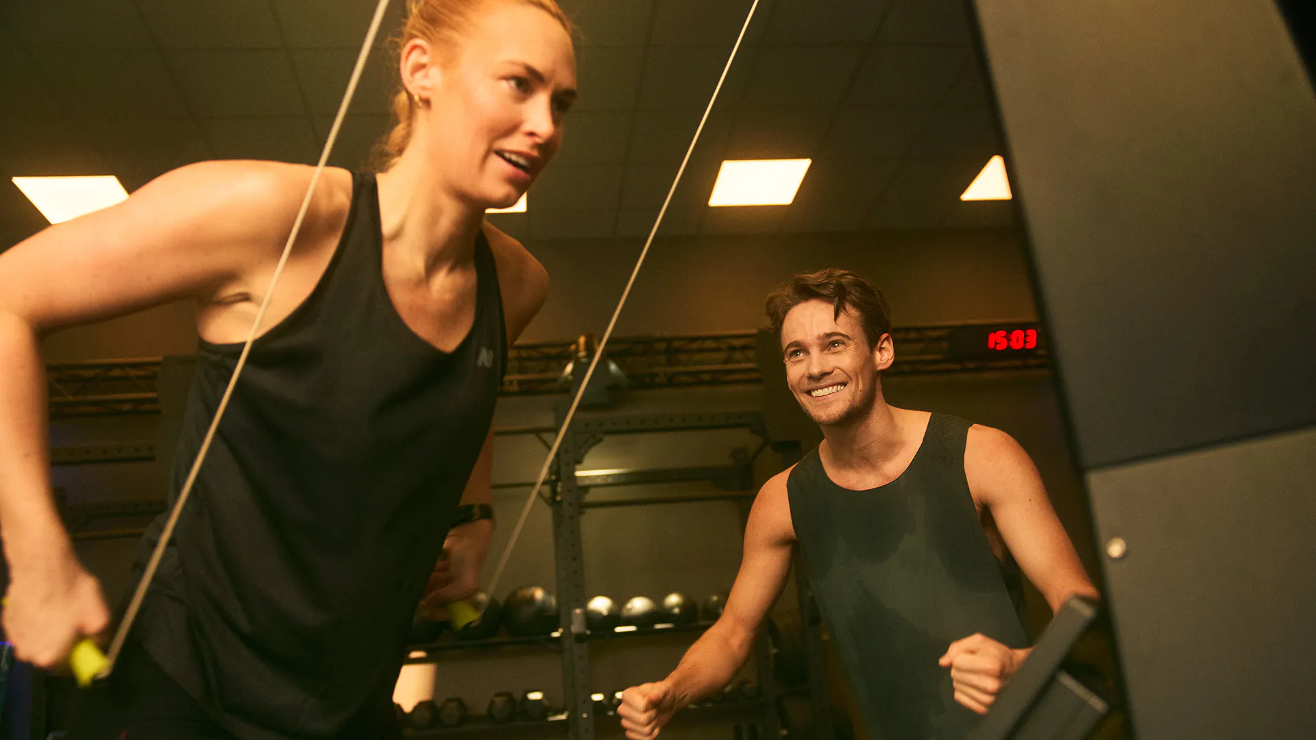 Glad kvinna och man tränar styrka tillsammans på STC-gym