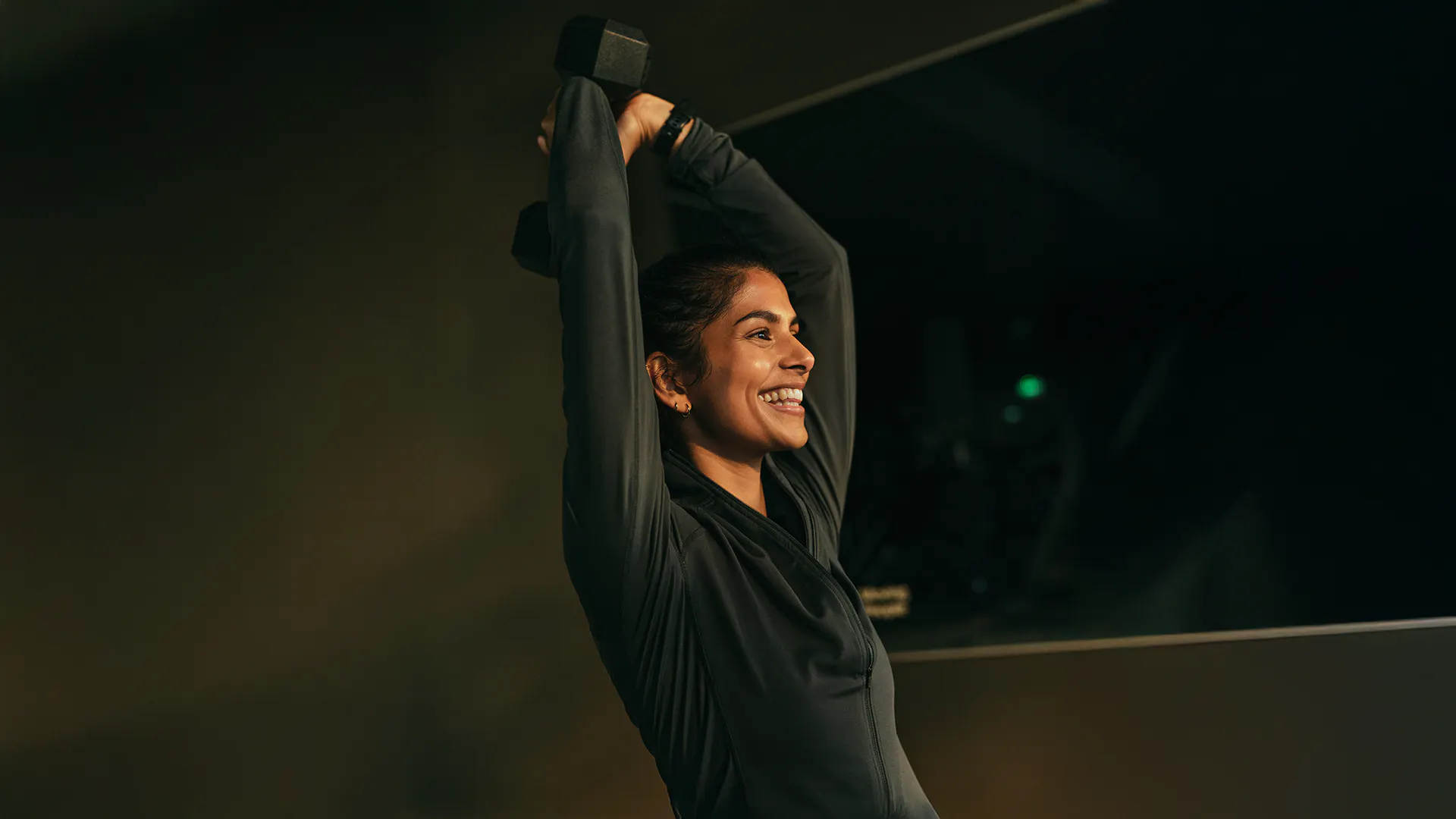 Glad mörkhårig kvinna stretchar armarna på gymmet