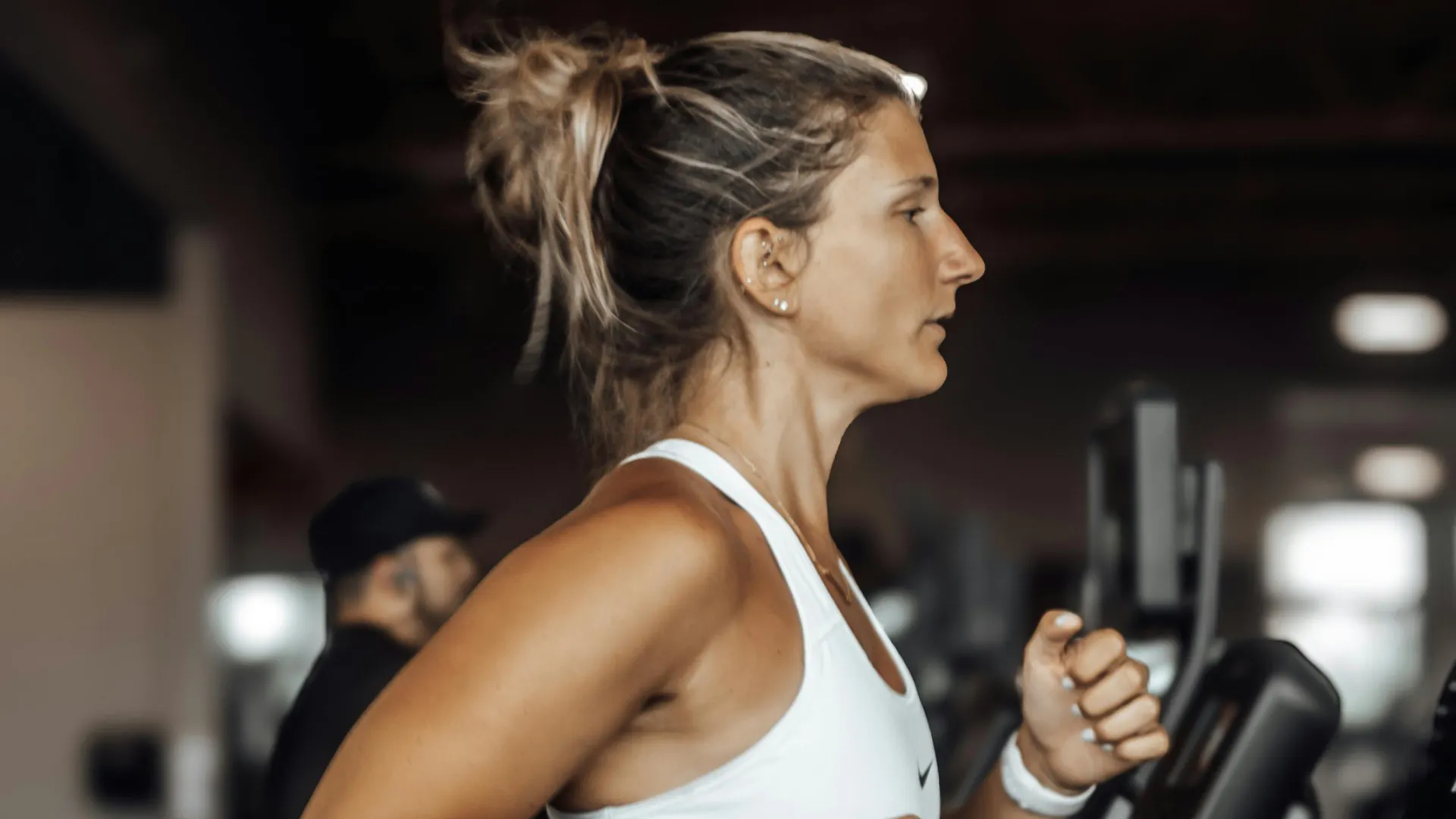 Blond kvinna med hästsvans och vitt träningslinne springer på löpband på gymmet