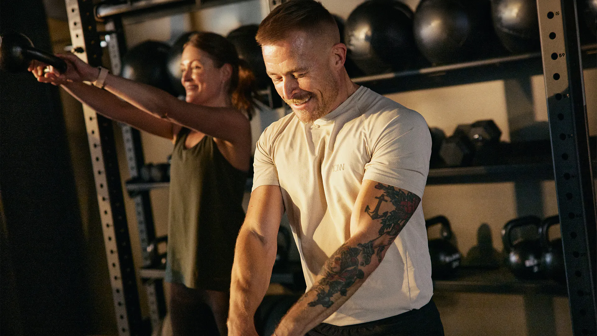 Glad man och kvinna tränar styrka på STC-gym med hantlar i bakgrunden