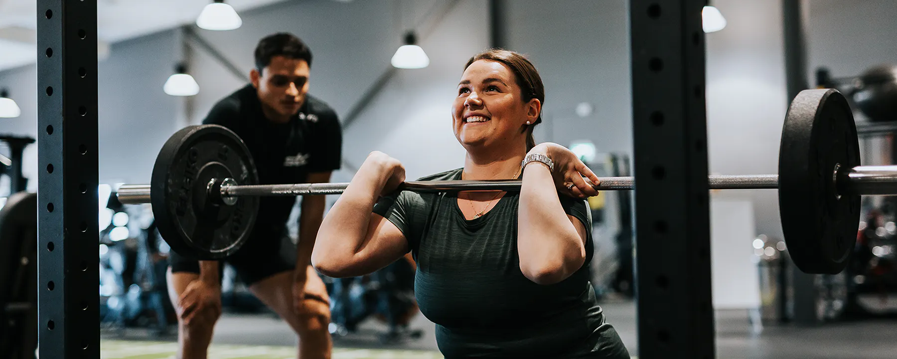 STC Livsstilsprogram, kvinna gör knäböj med en personlig tränare bakom sig på STC Training Club.