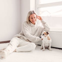 Frau sitzt zufrieden mit ihrem Hund an der warmen Heizung Dank des Licht und Steuerung System von Steinkühler in Leverkusen.