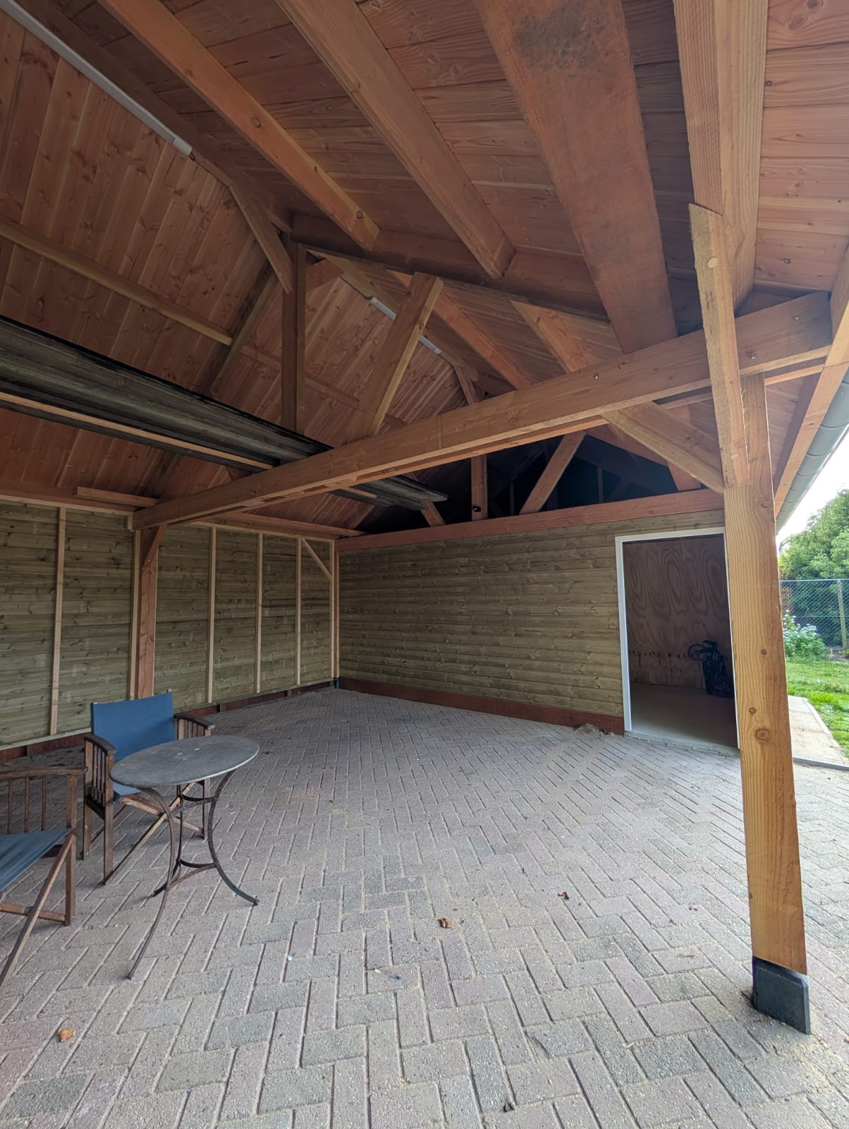 Binnenzijde van de overkapping met zichtbare houten balken en bestrating