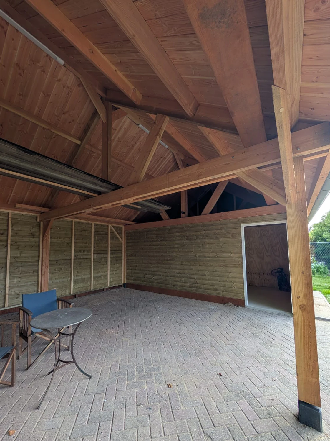 Binnenzijde van de overkapping met zichtbare houten balken en bestrating