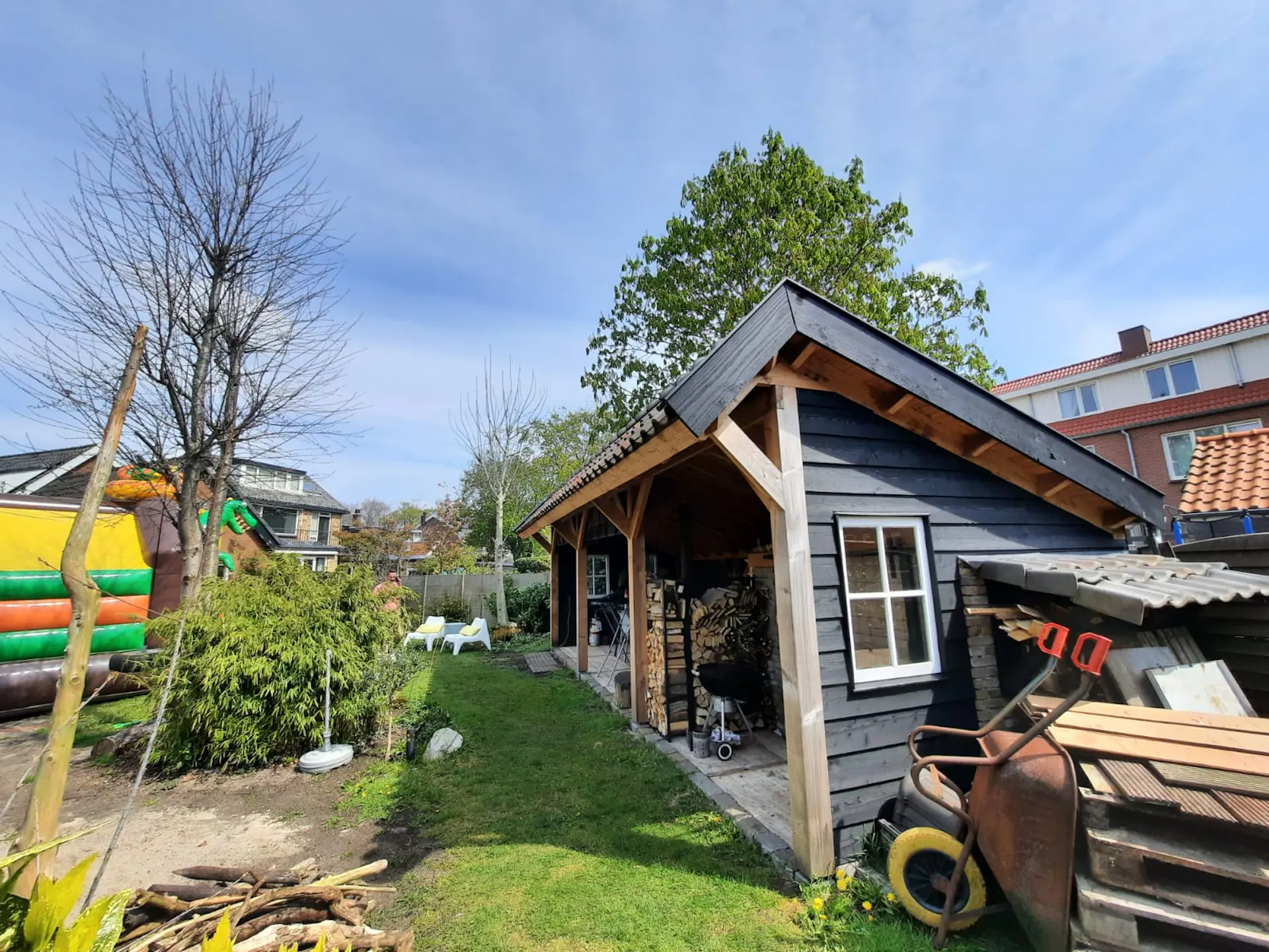Brede houten veranda langs zwarte schuur als onderdeel van de tuin