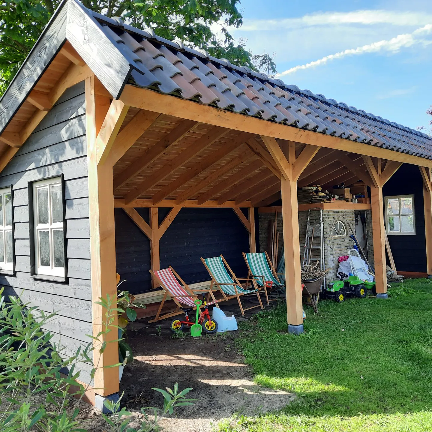 Houten veranda met zichtbare spanten en pannendak aan zwarte schuur