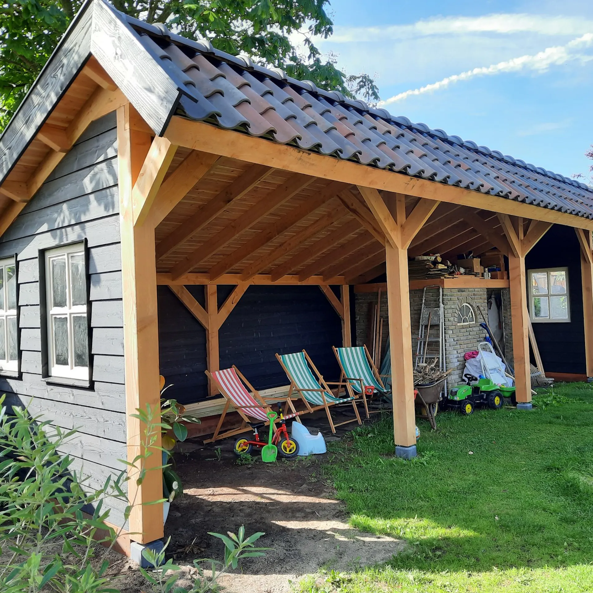 Houten veranda met zichtbare spanten en pannendak aan zwarte schuur