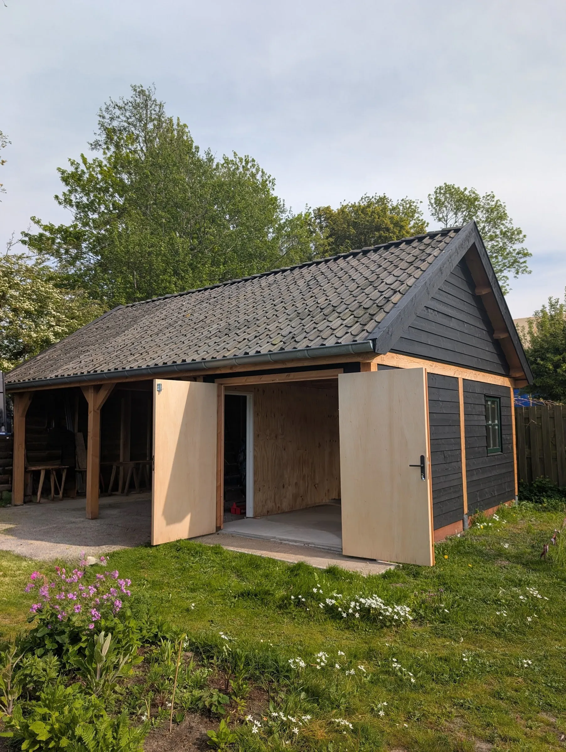 Nieuwe zwarte houten schuur met open deuren en pannendak in de tuin