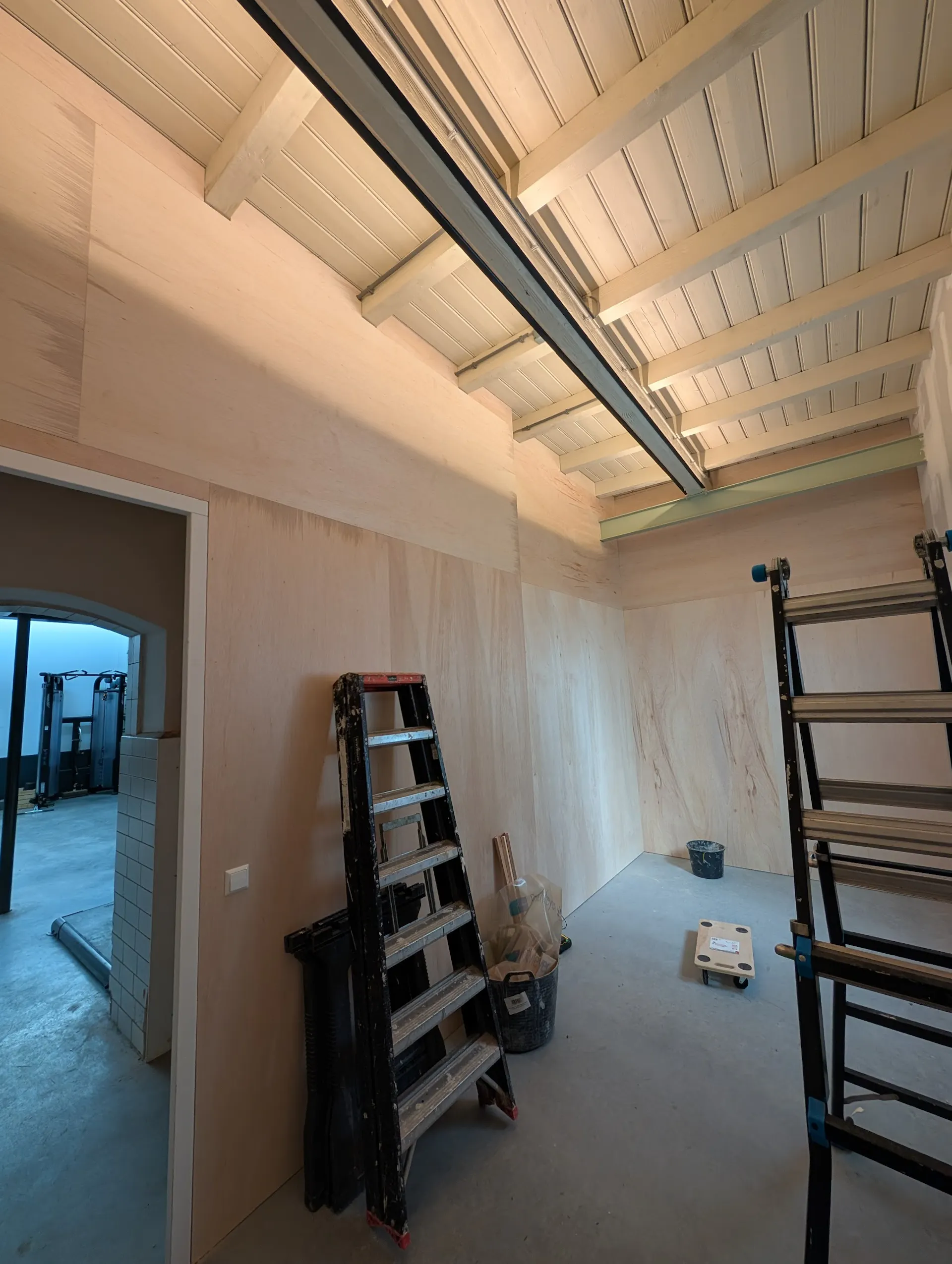 Hoge ruimte met multiplex wandafwerking en wit houten balkenplafond