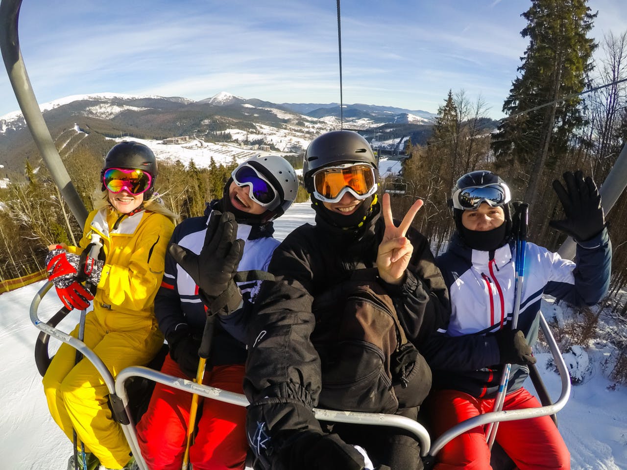 Happy young friends skiers on ski lift ride up on ski slope at snowy mountain