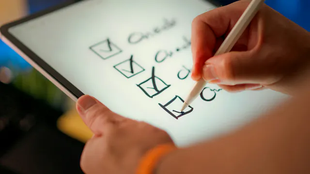 A close-up of someone writing a checklist on a tablet.
