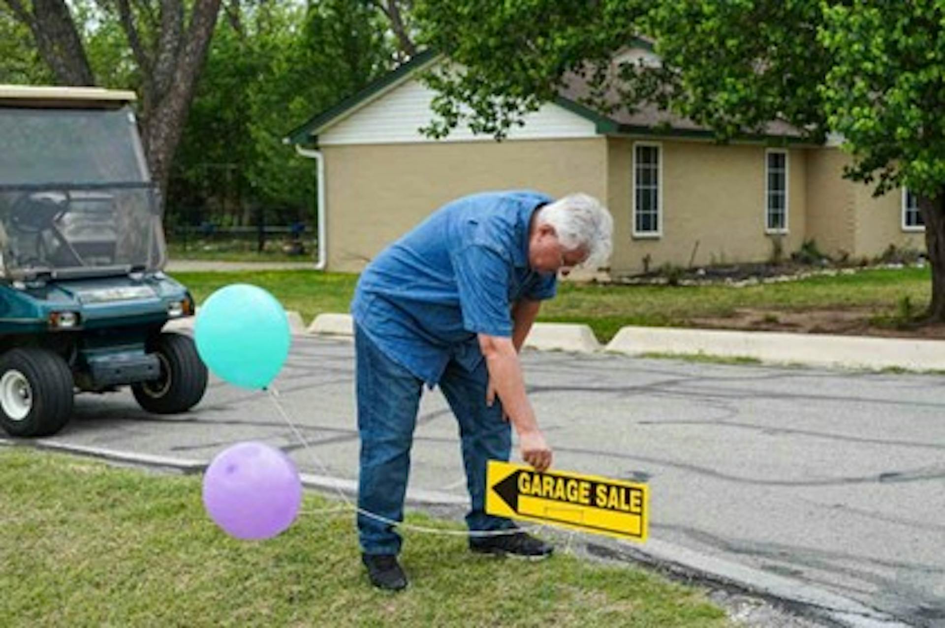 A man places a garage sale sign with balloons on a street corner