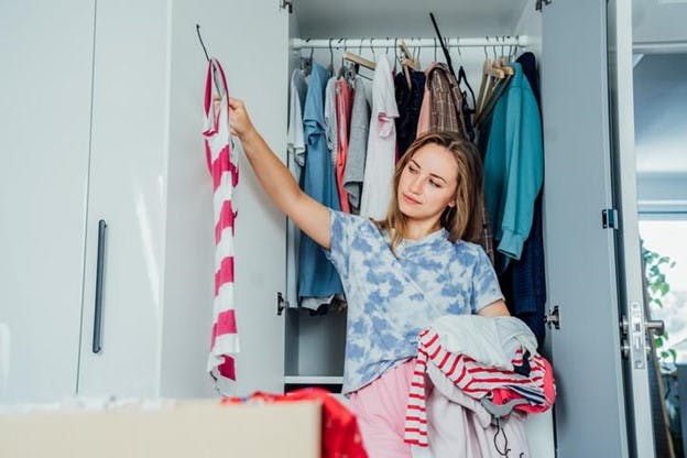 A woman holds up a striped t-shirt while holding several more in another arm, deciding if she will keep it.