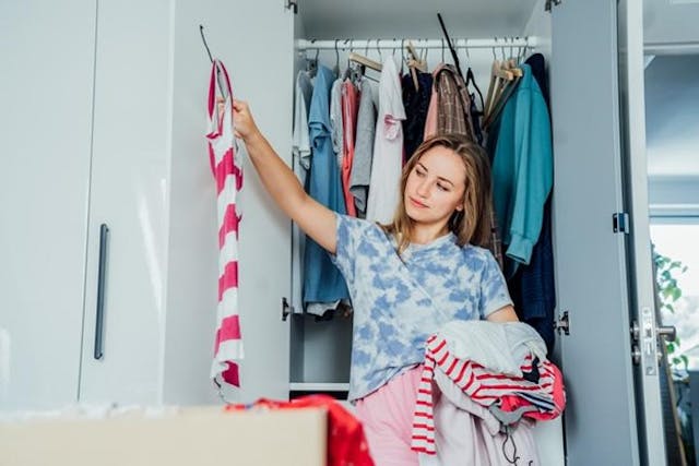 A woman holds up a striped t-shirt while holding several more in another arm, deciding if she will keep it