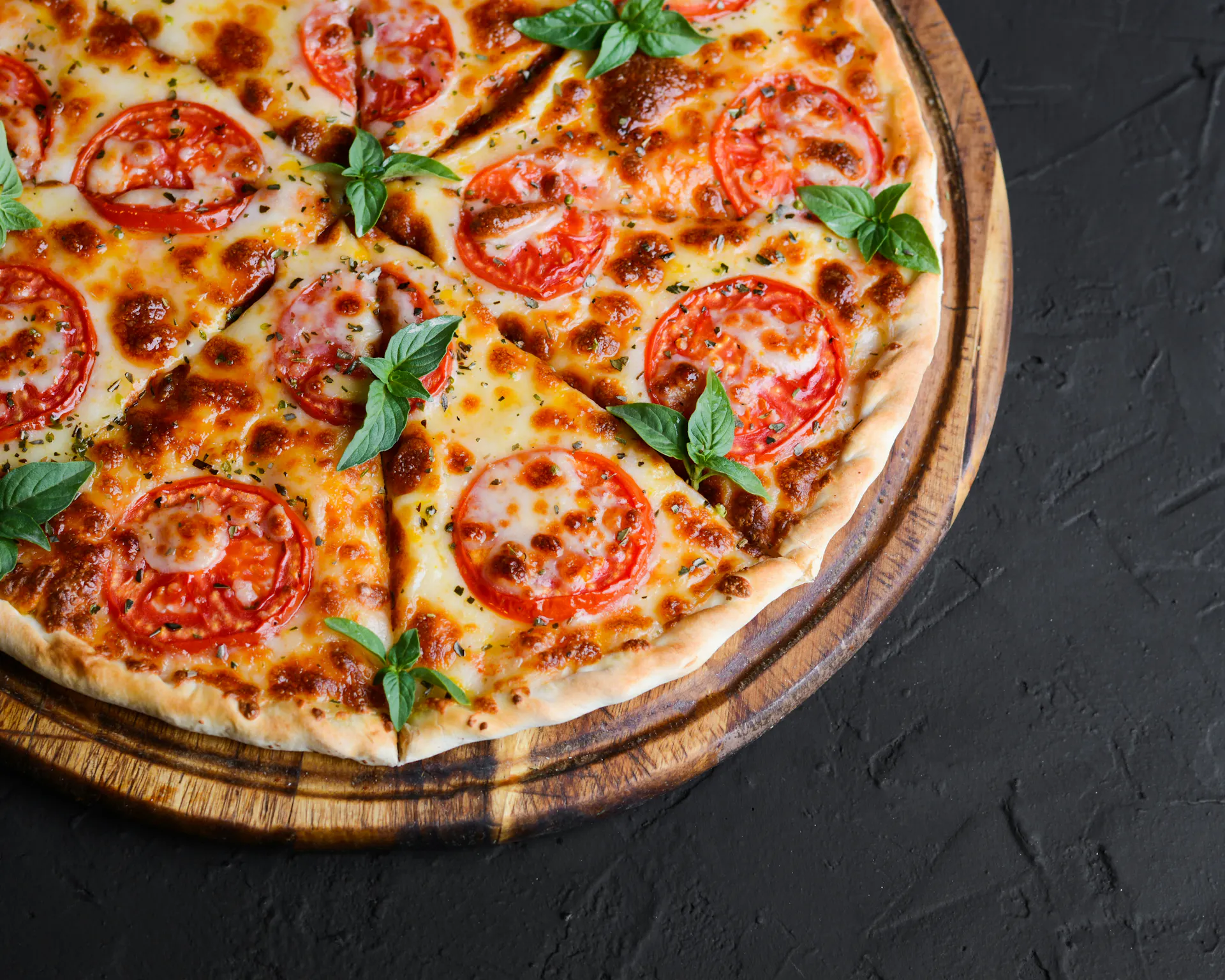 A close-up of an Italian pizza with pepperoni and basil served on a wooden pan on a black table.