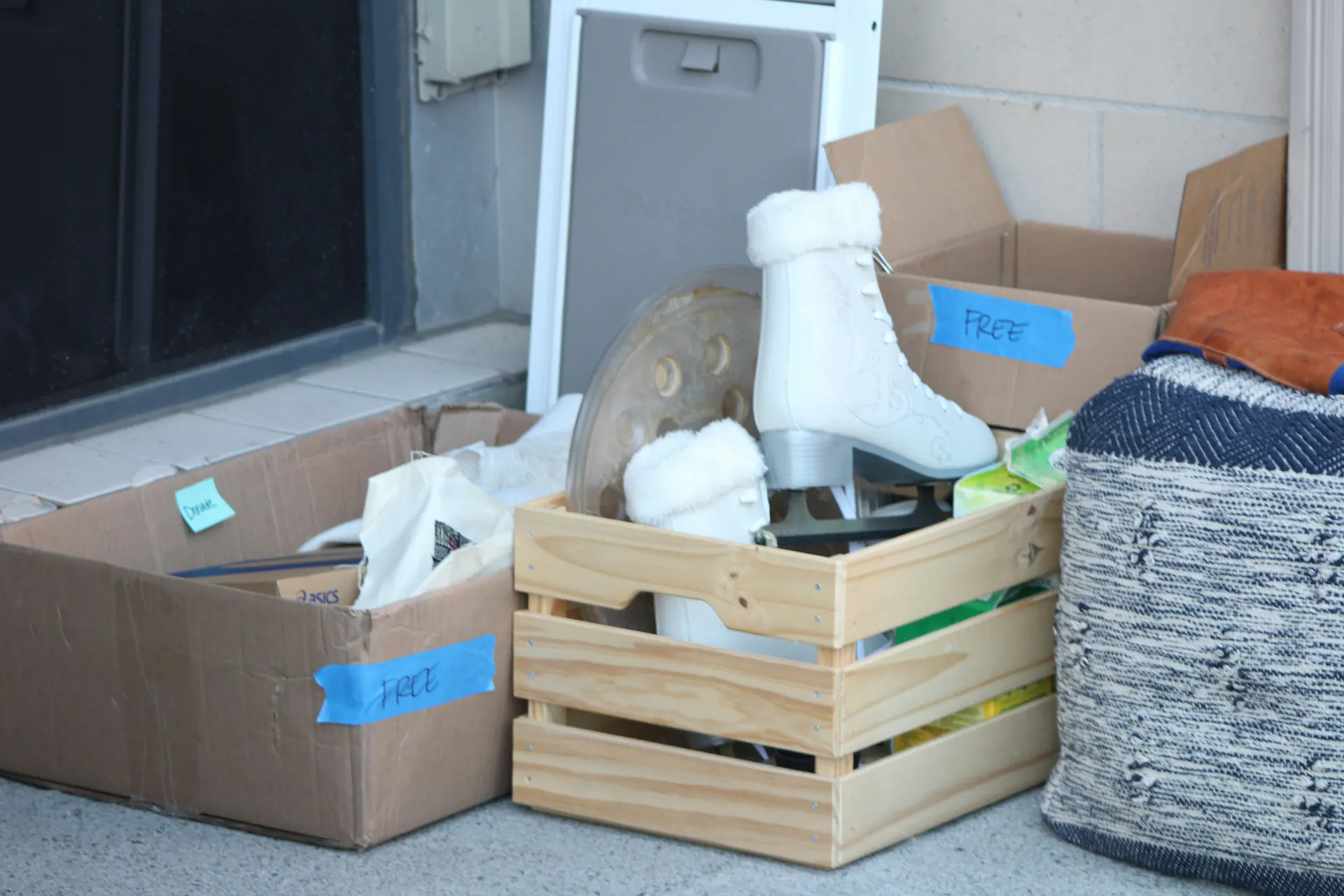 Several boxes full of free/donation items on the sidewalk near the front of a house.