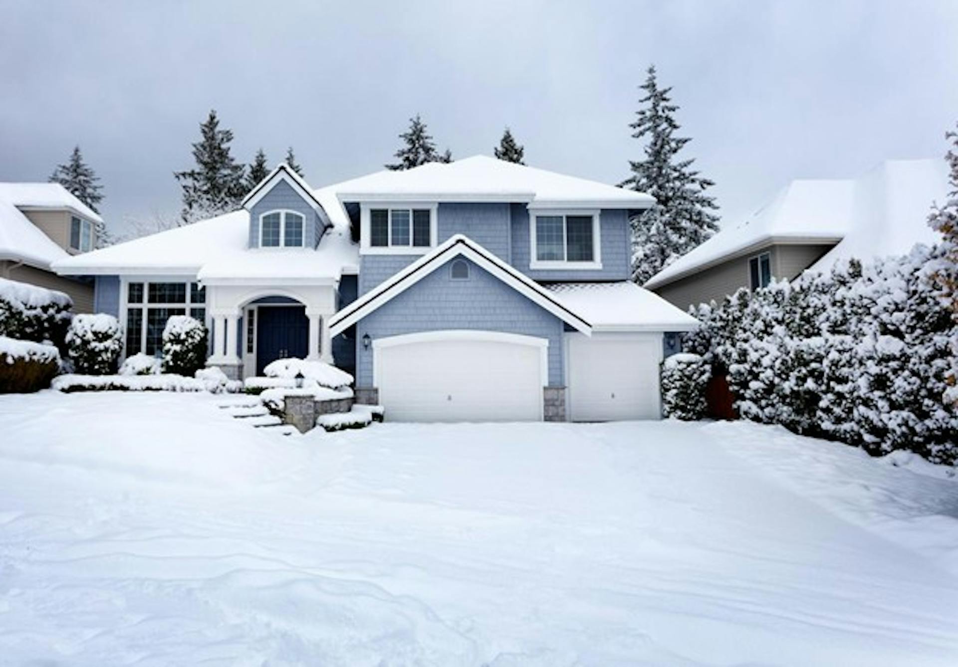 a snow-covered blue house sits in a suburban winter environment