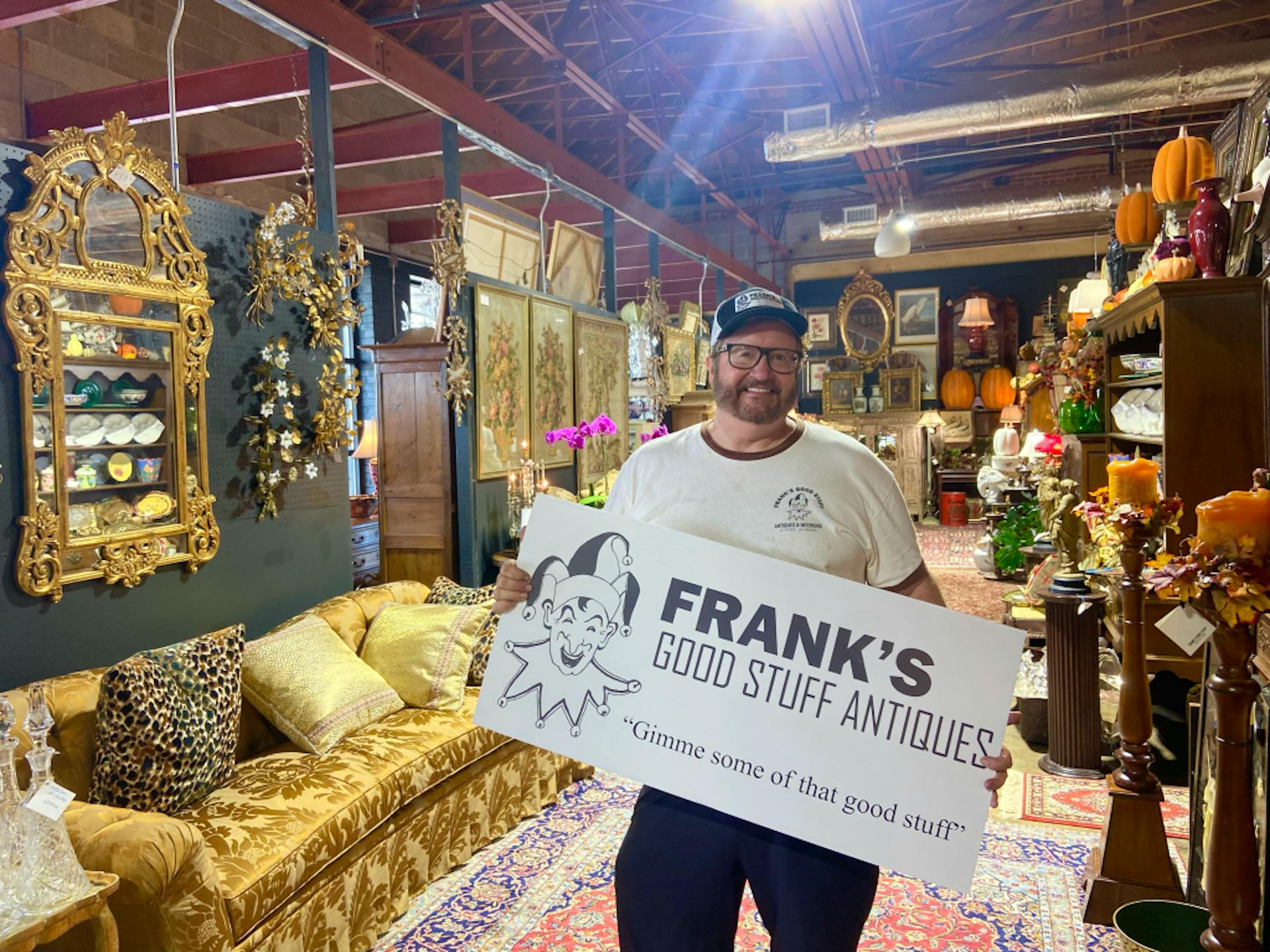 owner of Frank’s Good Stuff in Athens holding sign in Antique store