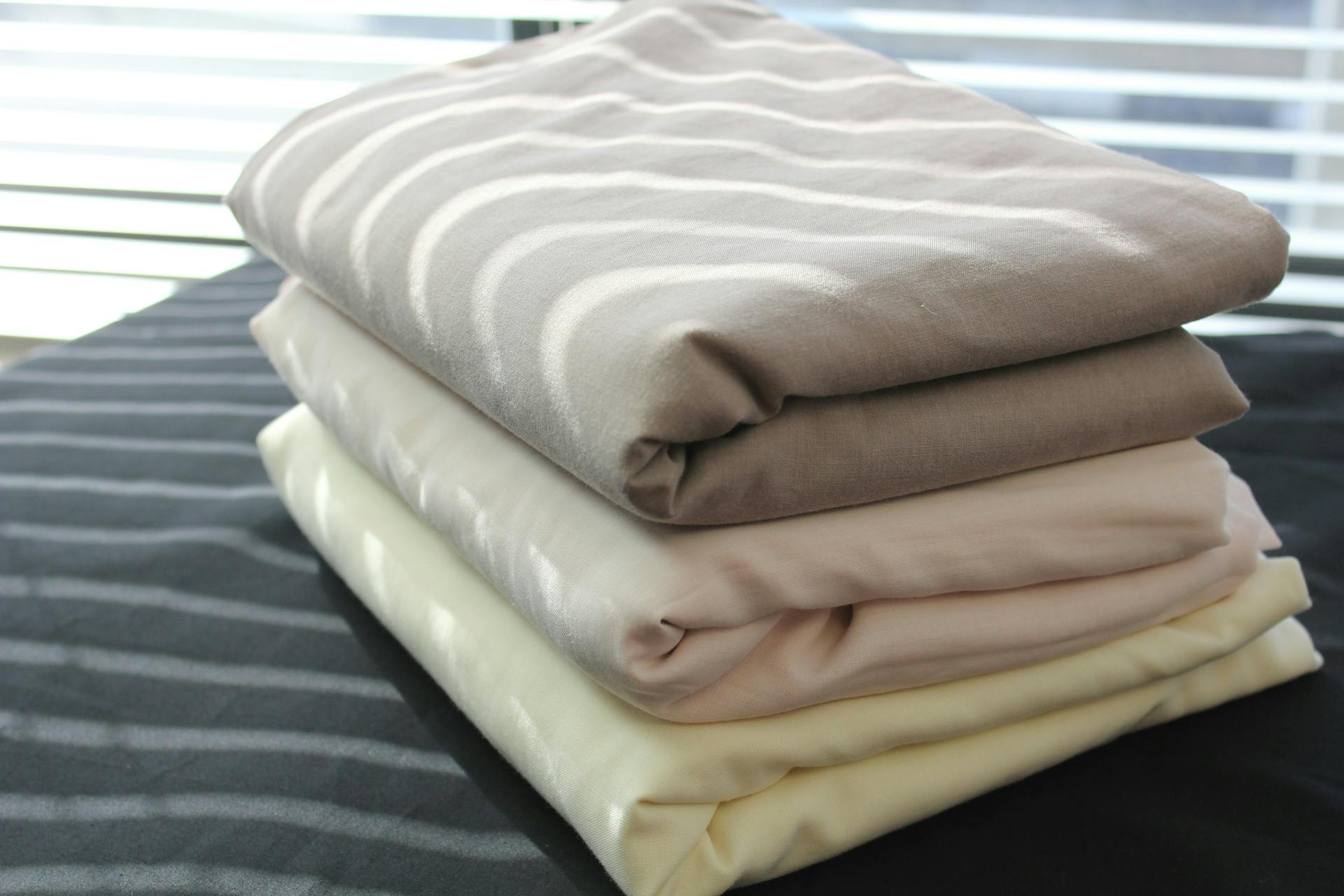 A stack of three sets of linens sitting on the corner of a bed}