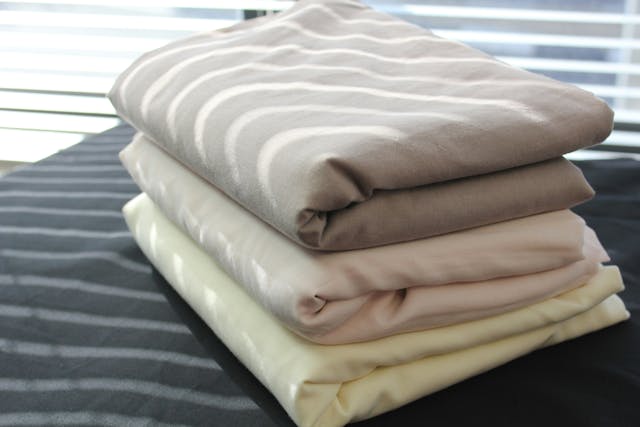 A stack of three sets of linens sitting on the corner of a bed}