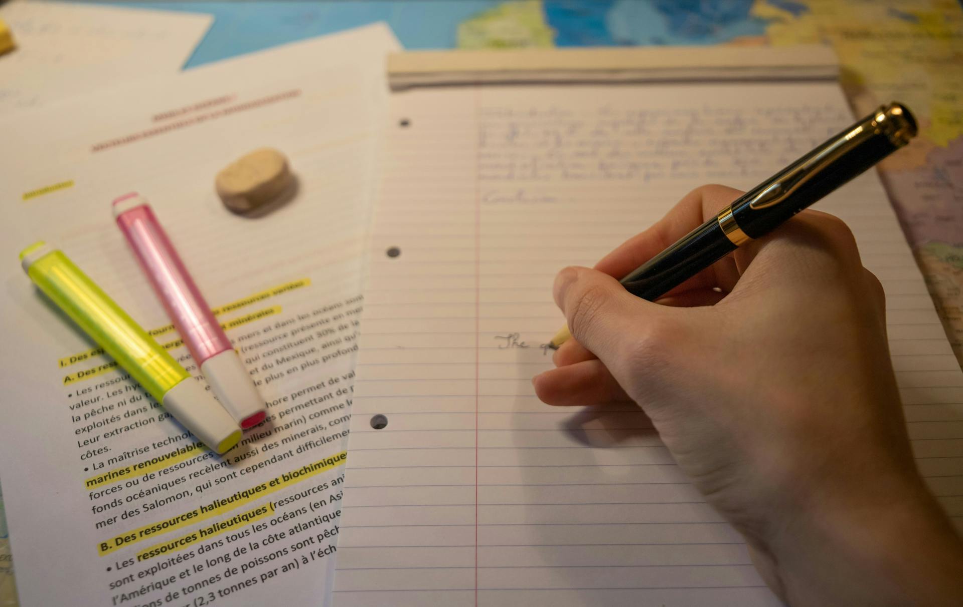 A close-up of a student doing homework with a pencil and several highlighters