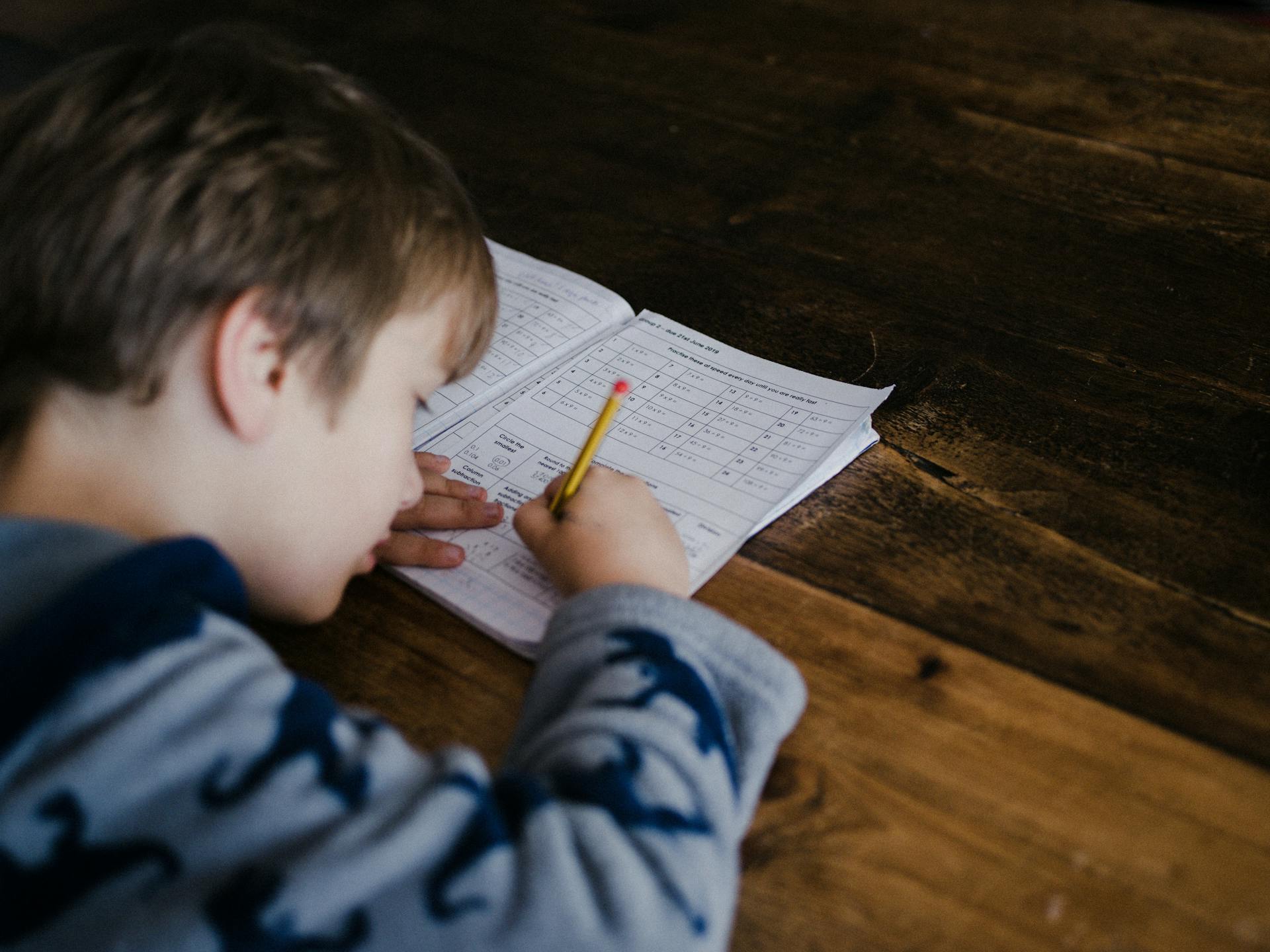A young boy working on homework at a wooden table