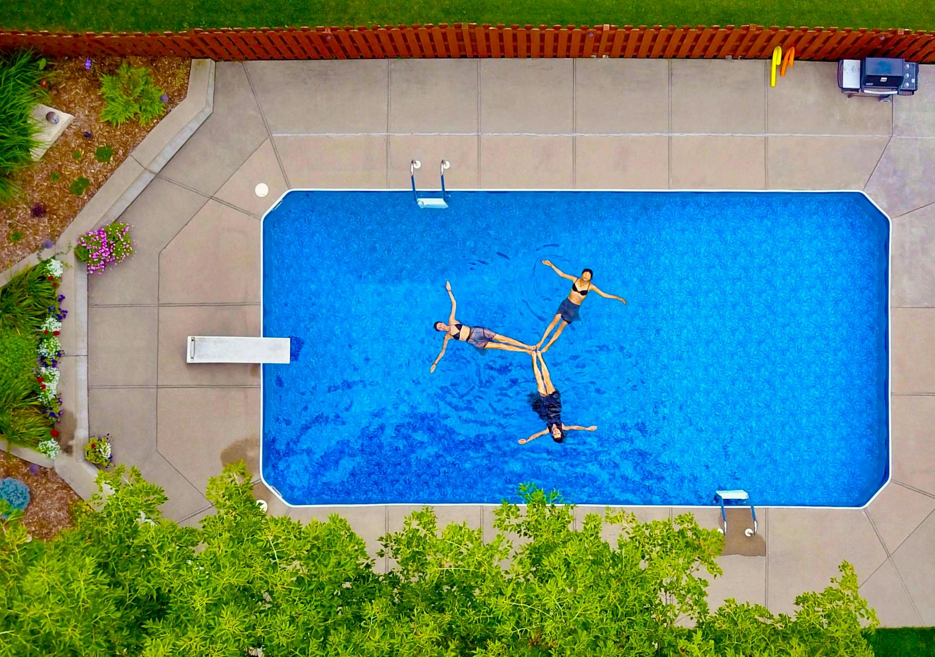 An aerial shot of three people floating in a swimming pool