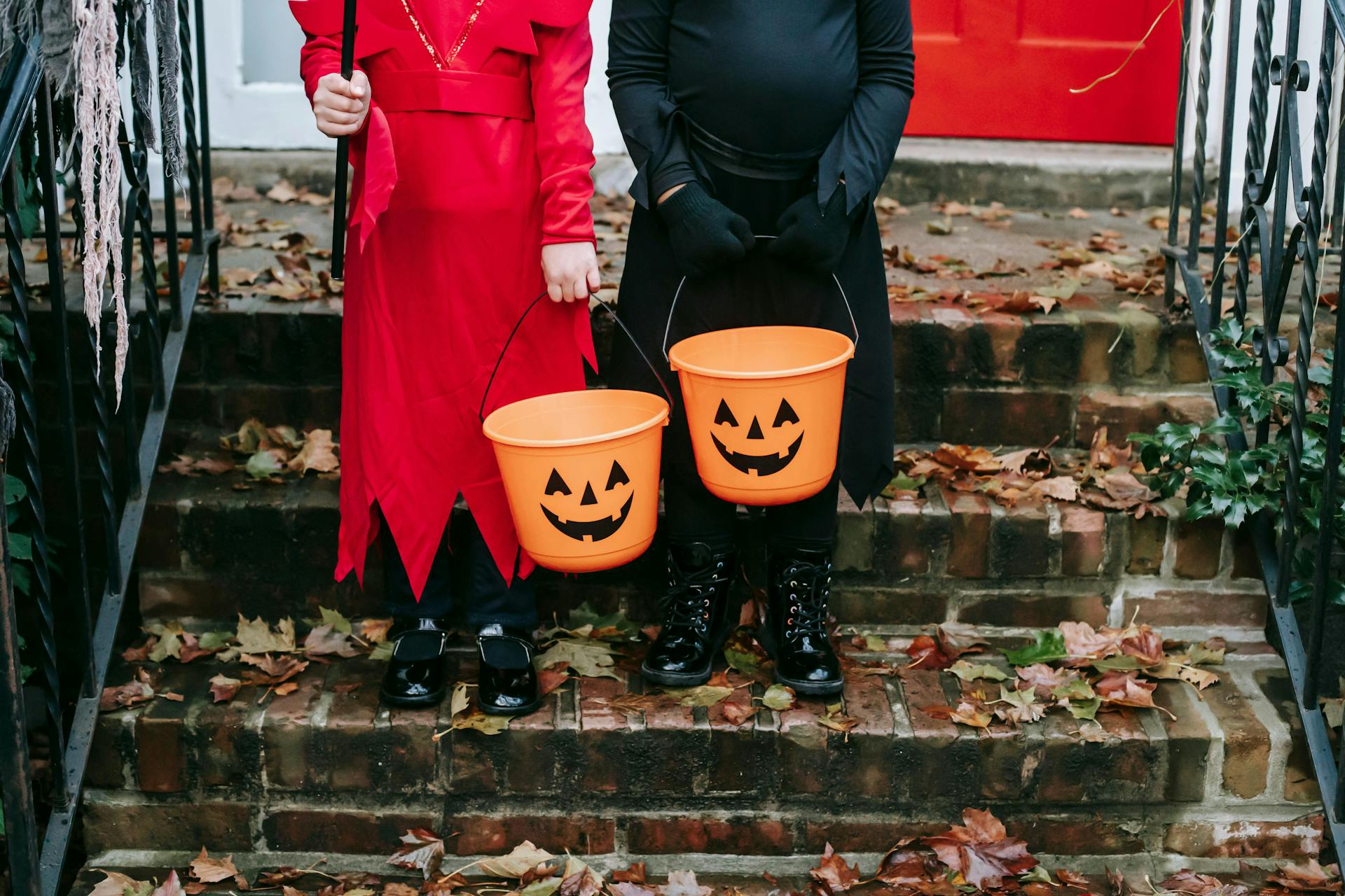 Two kids in costumes on a front porch holding trick-or-treating buckets
