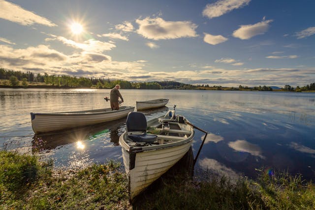 three canoes on the bank of a lake with a man standing in one 