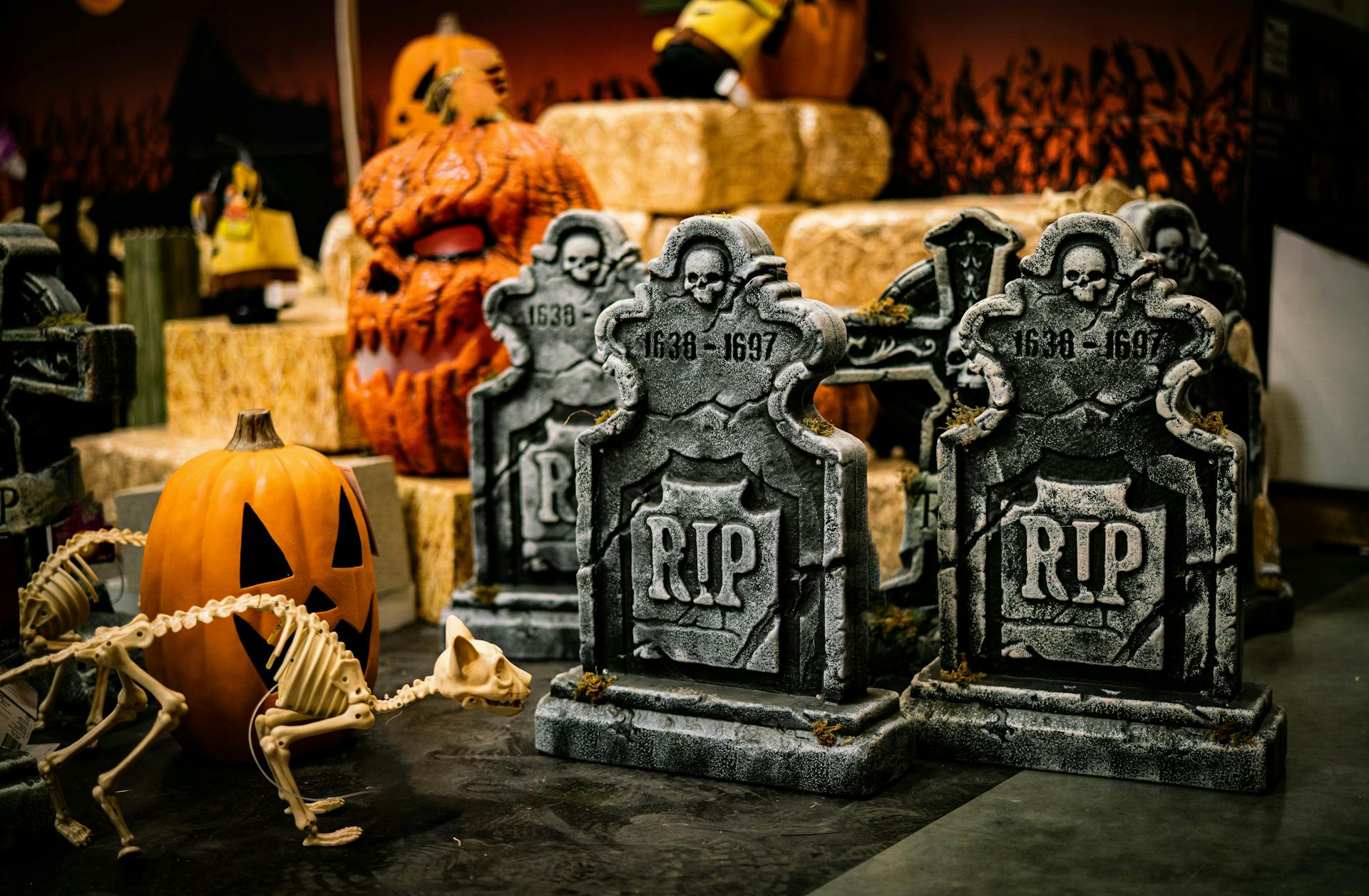 A group of Halloween decorations such as foam tombstones, pumpkins, a cat skeleton, and hay bales in storage