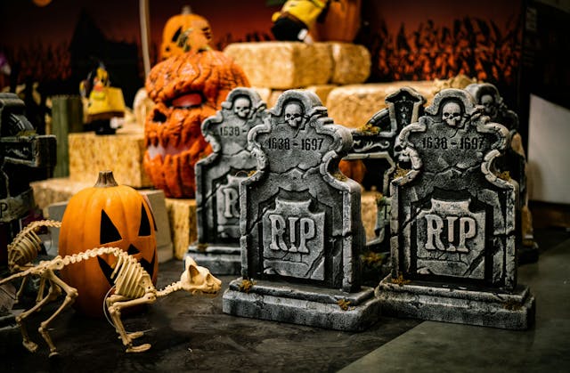 A group of Halloween decorations such as foam tombstones, pumpkins, a cat skeleton, and hay bales in storage