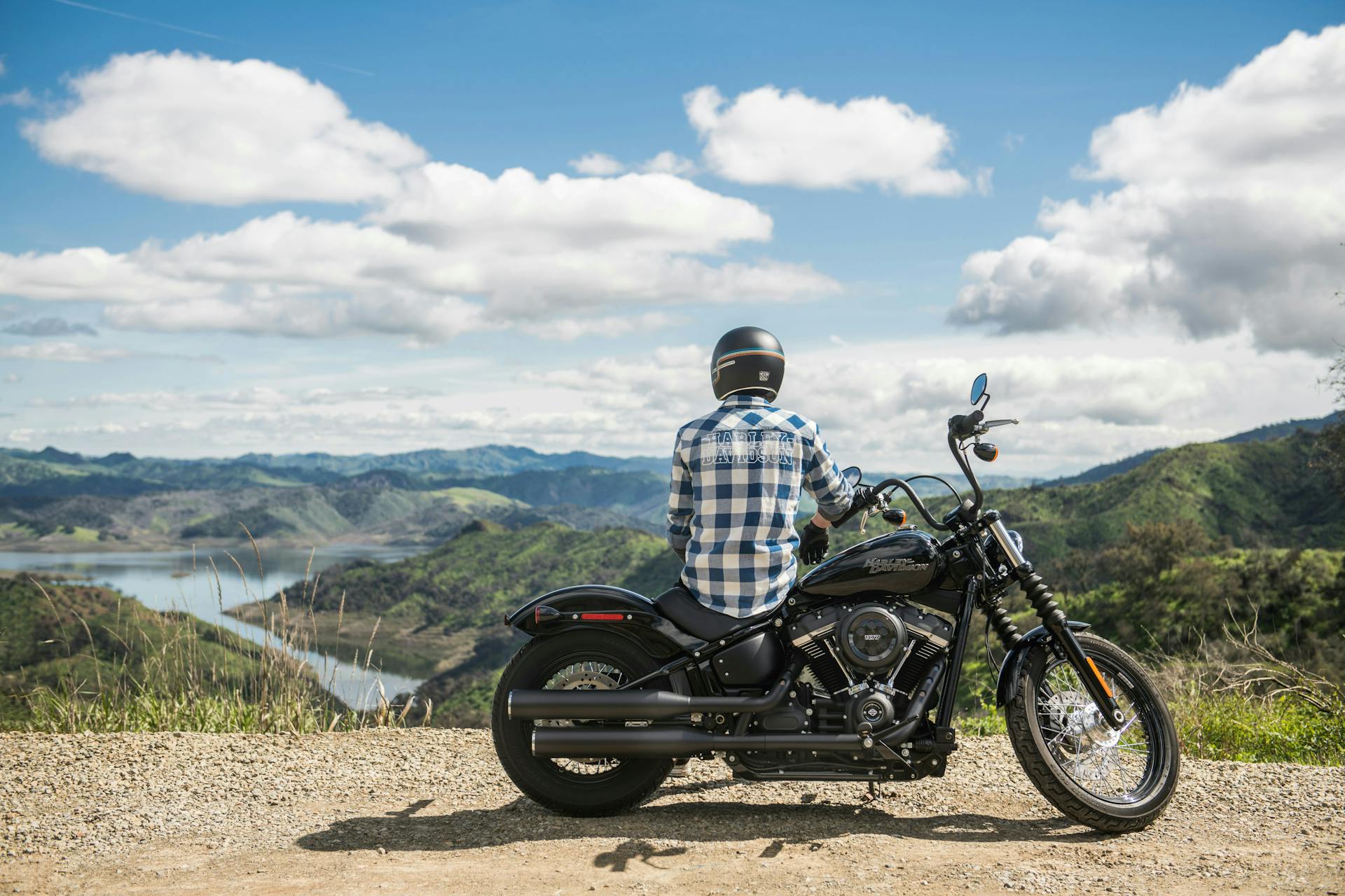 A person sitting on a Harley Davidson motorcycle looking out at a mountain range with a lake