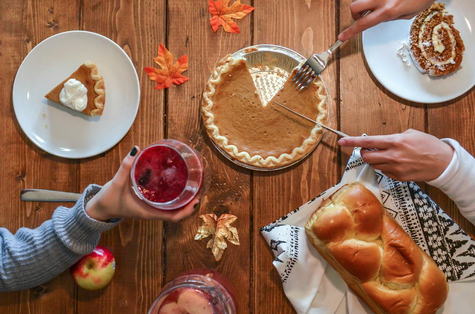 An ariel shot of someone slicing a pumpkin pie on a wooden table with fall decorations