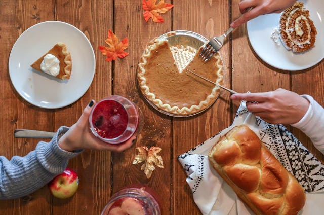 An ariel shot of someone slicing a pumpkin pie on a wooden table with fall decorations