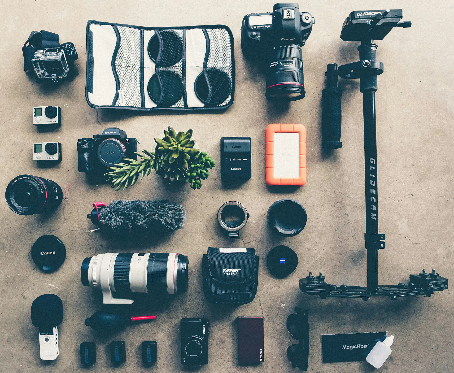 A variety of photography equipment, including lenses, camera bodies, batteries, and more, set out on the floor.