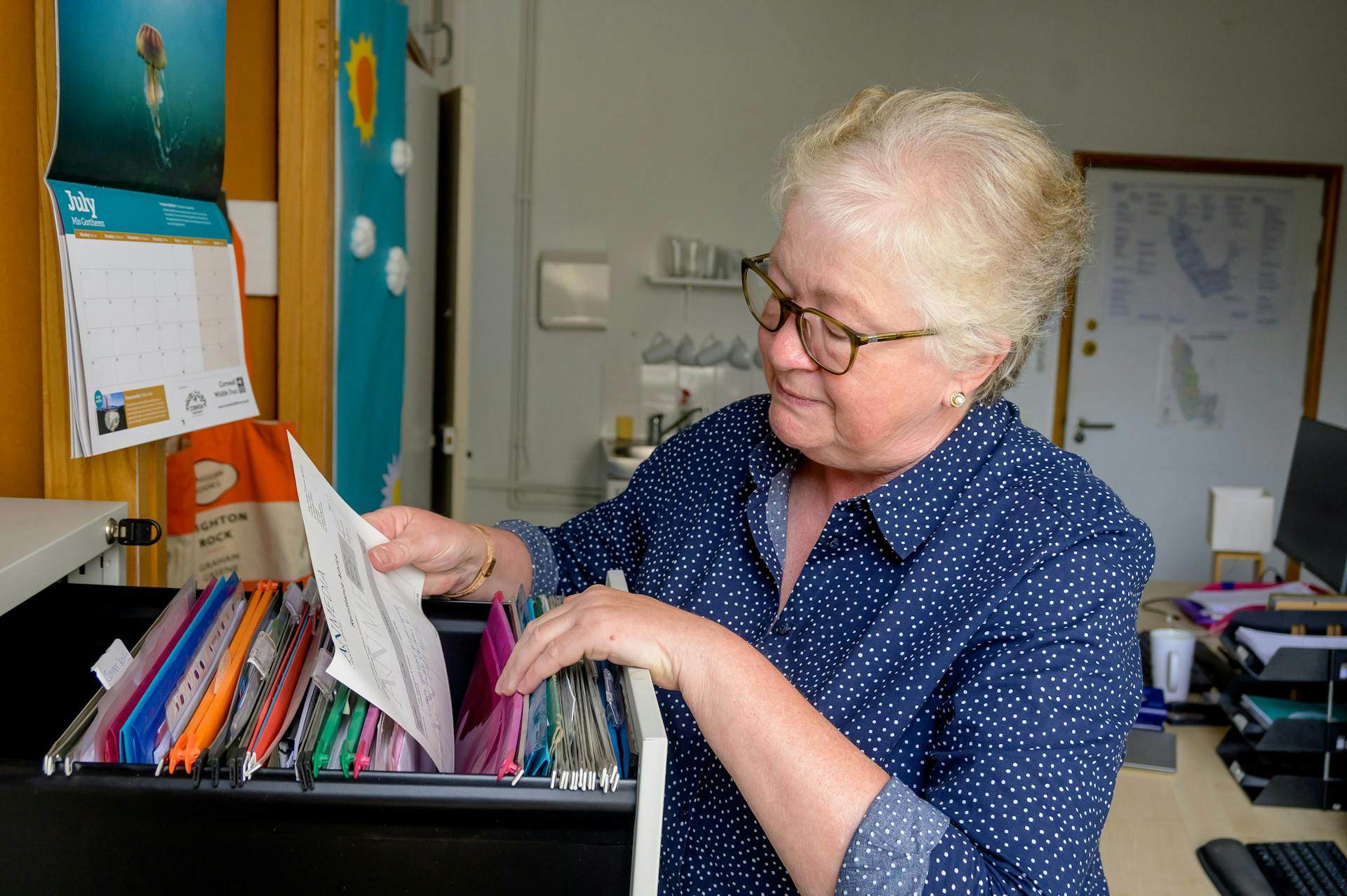An older woman sorting through a filing cabinet.