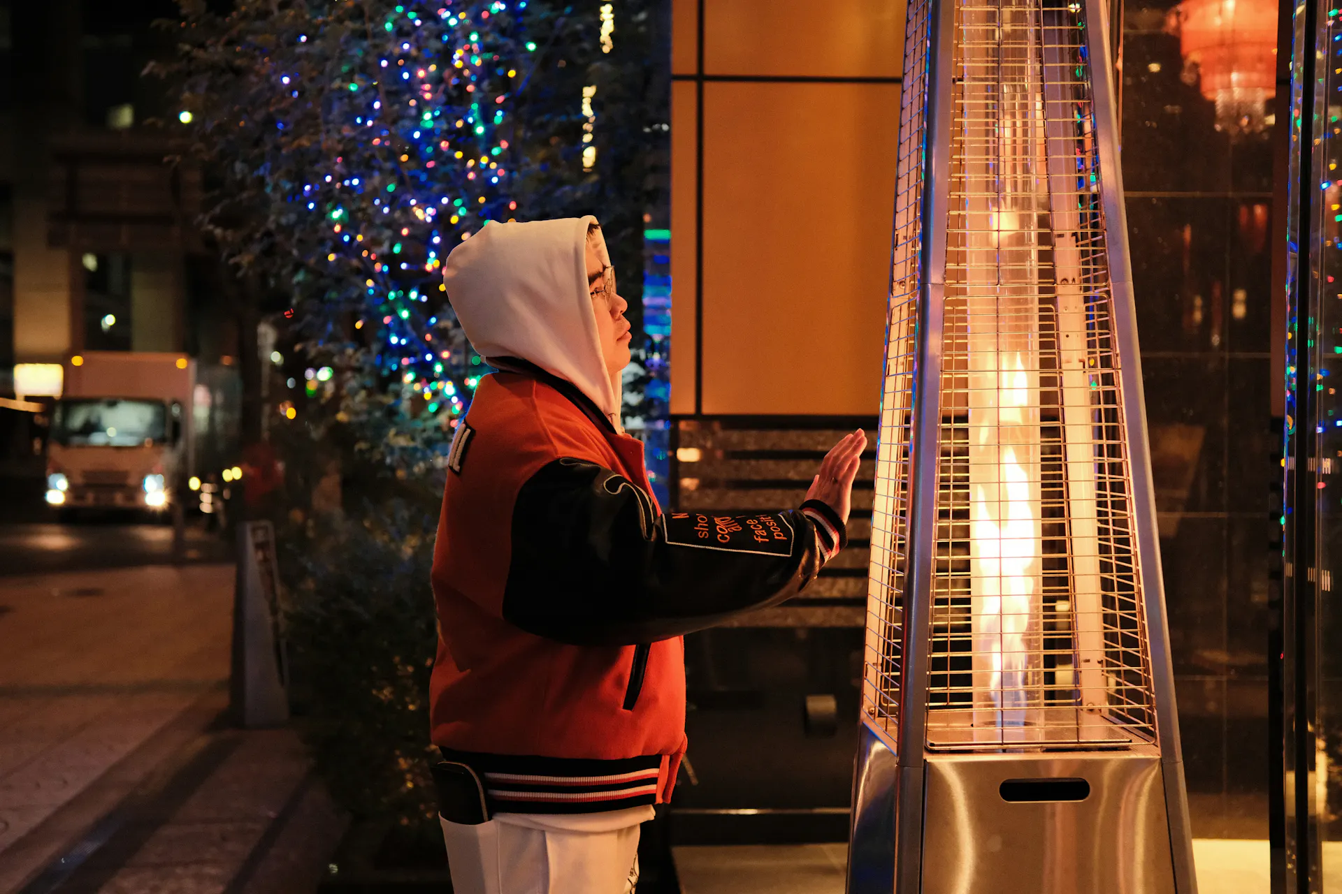 A person bundled up and warming next to an outdoor patio heater.