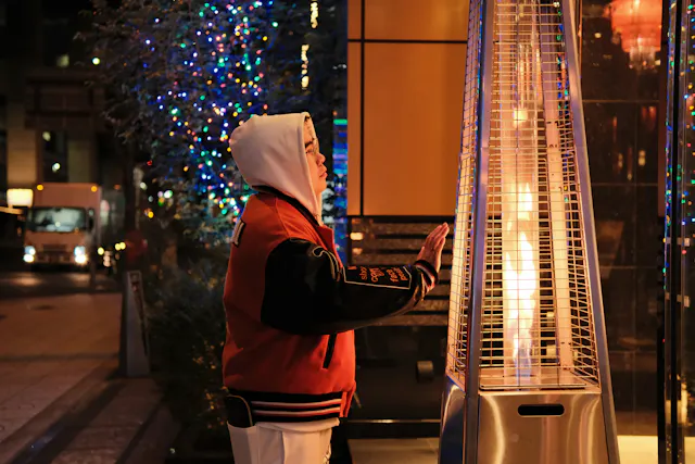 A person bundled up and warming next to an outdoor patio heater.