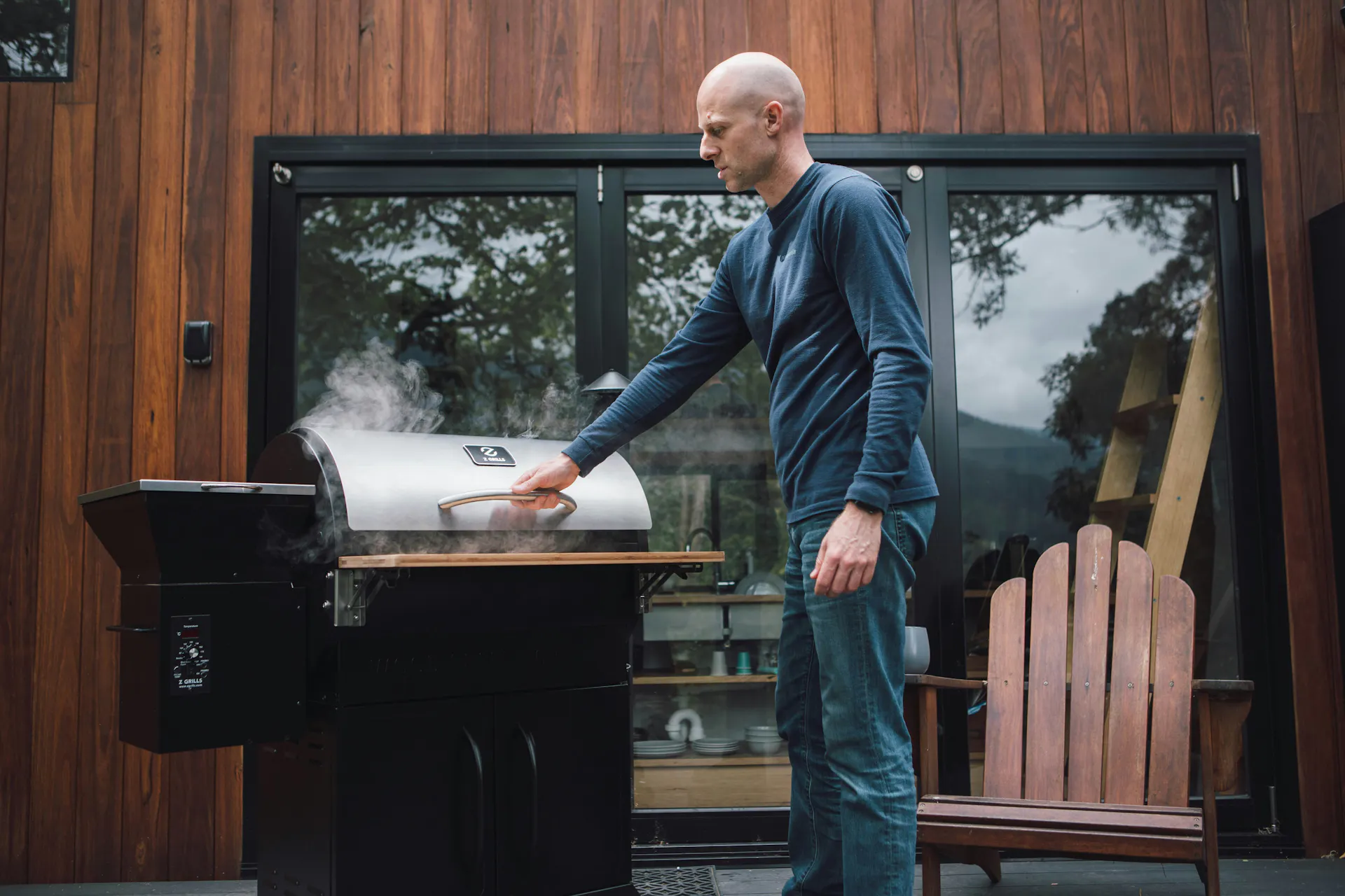 A man in a black shirt opening a grill on his patio.
